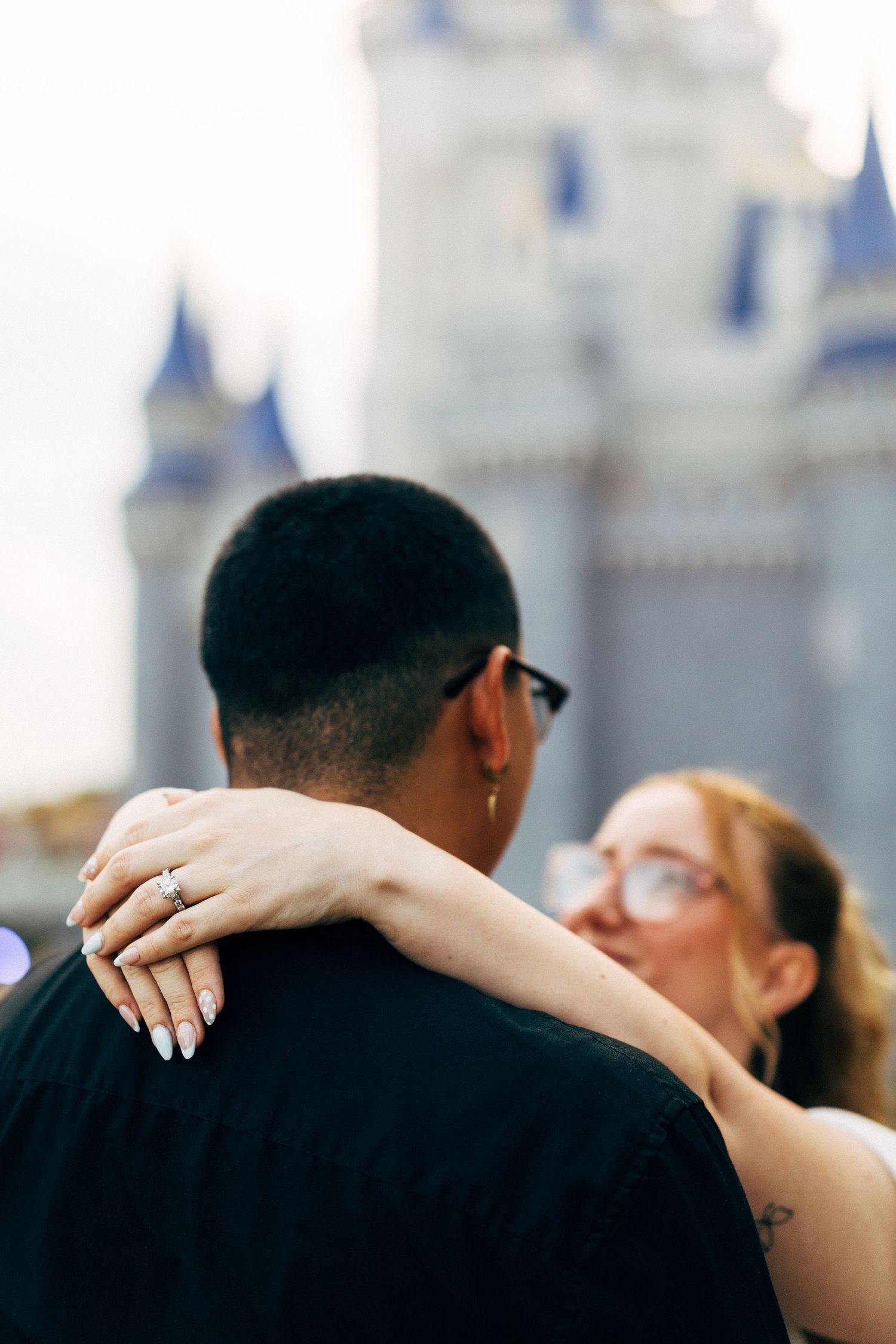 Couple embracing in front of Cinderella Castle at Disney World, woman showing engagement ring on her hand.
