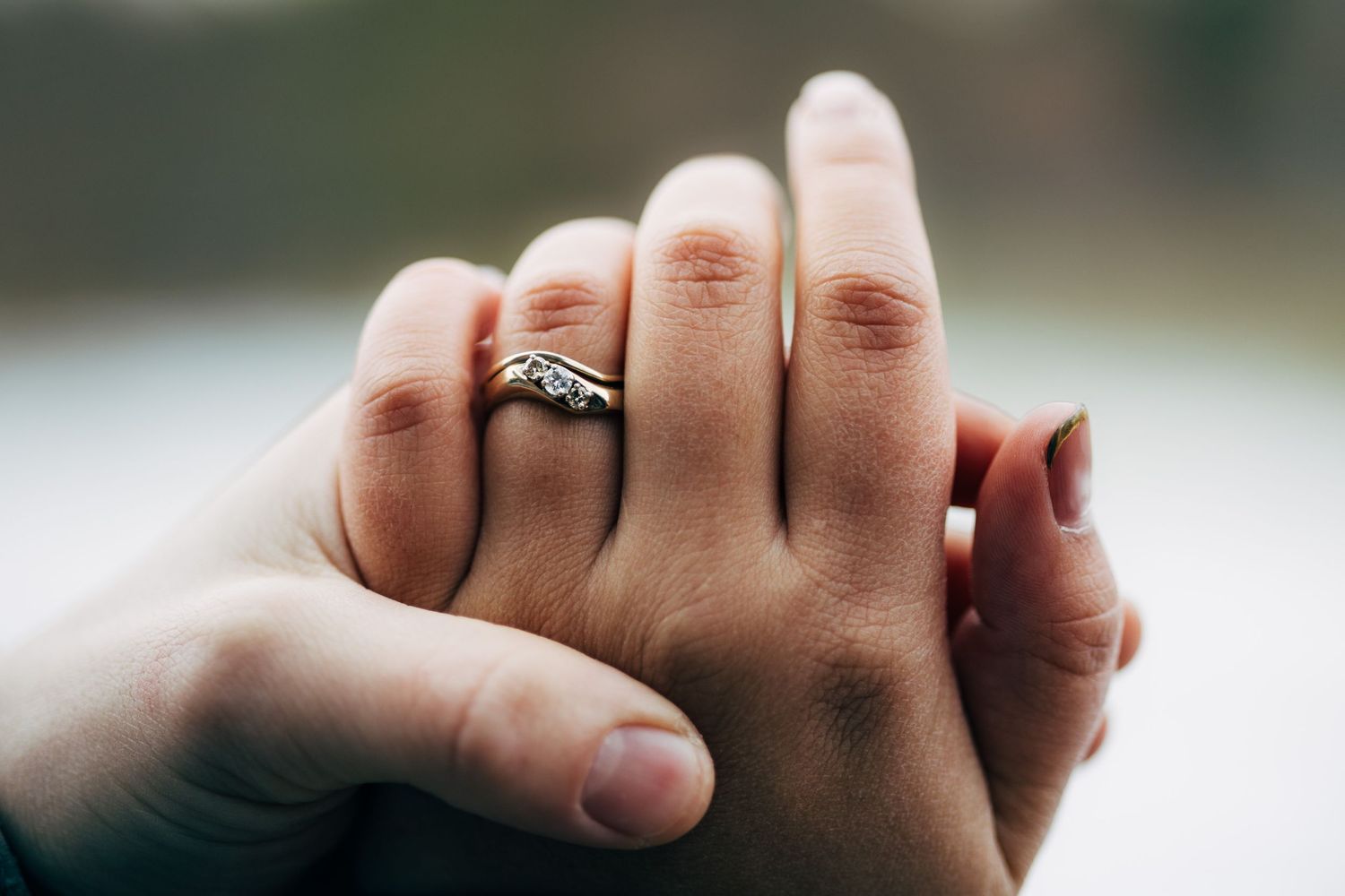 Close up of hands with engagement ring during romantic outdoor moment.