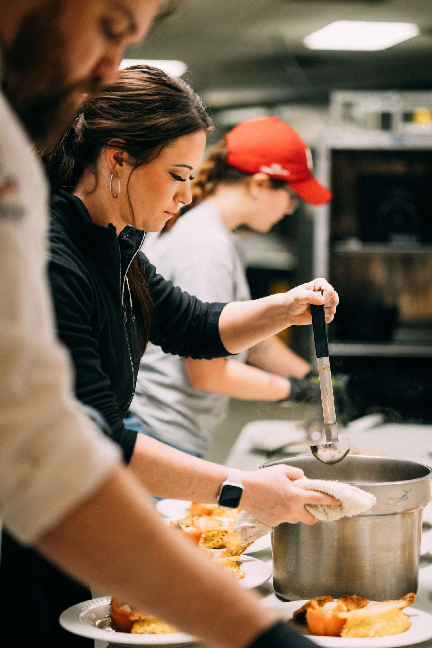 Chefs working in a professional kitchen, plating dishes with ladles and serving spoons in a busy restaurant.