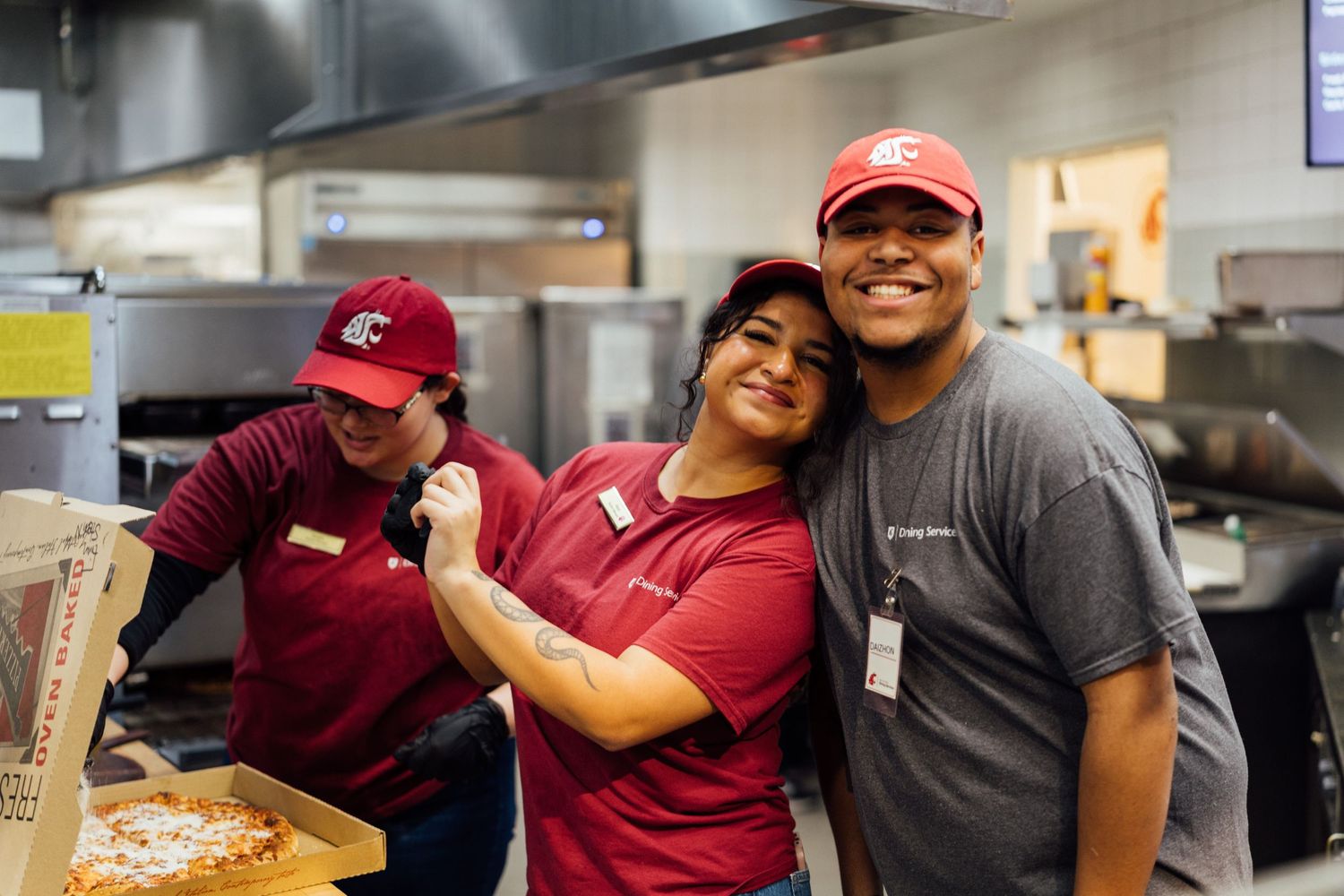 Kitchen staff members working together and sharing smiles in a busy restaurant kitchen.