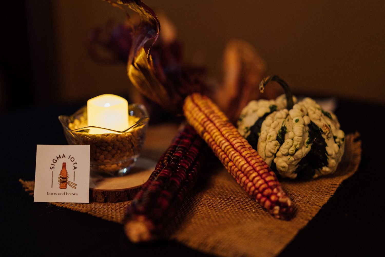 Decorative fall display with Indian corn and gourds lit by warm candlelight.