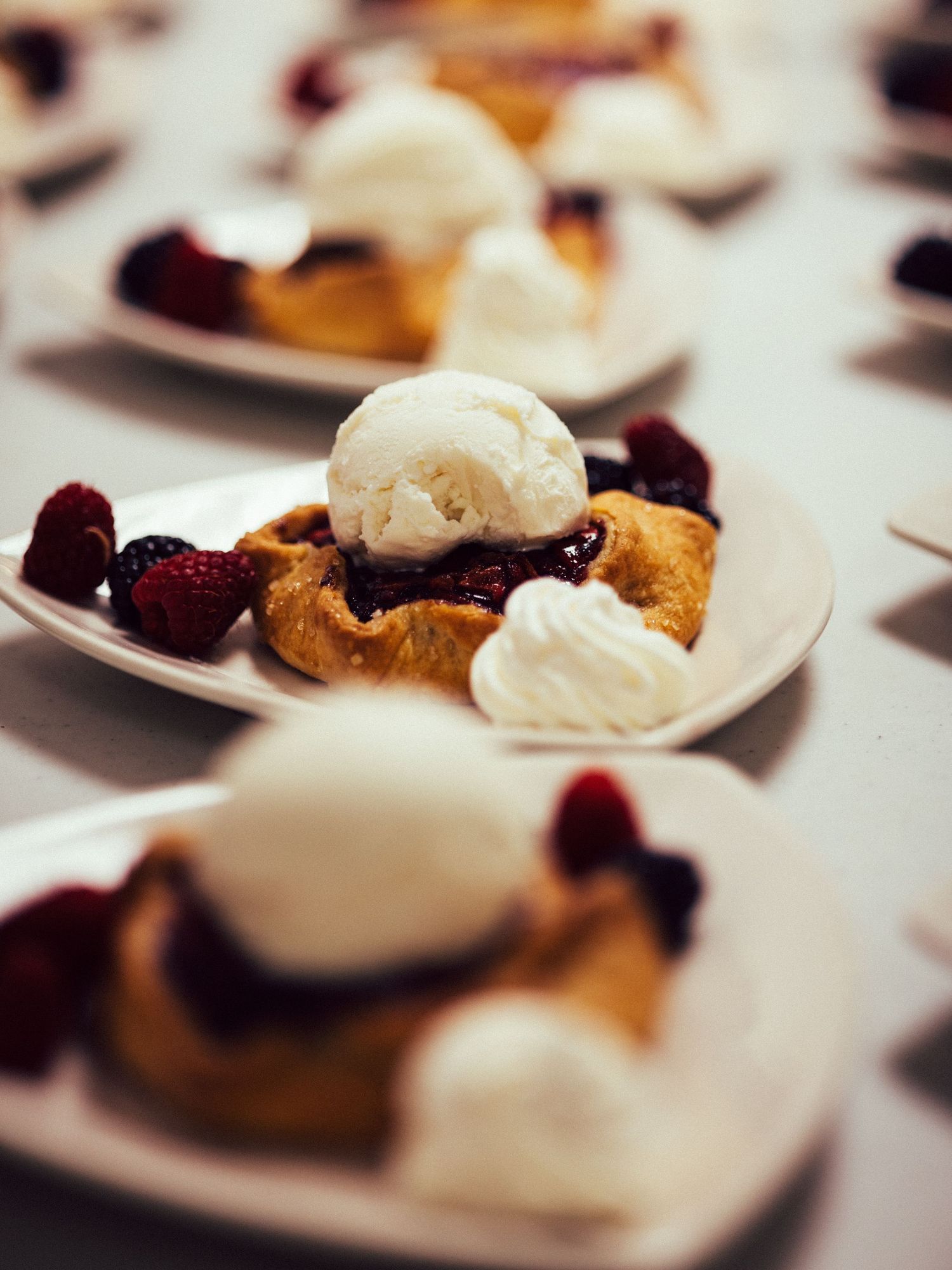 Elegant dessert plates with berry pie, fresh raspberries, ice cream scoops, and whipped cream served at an event.
