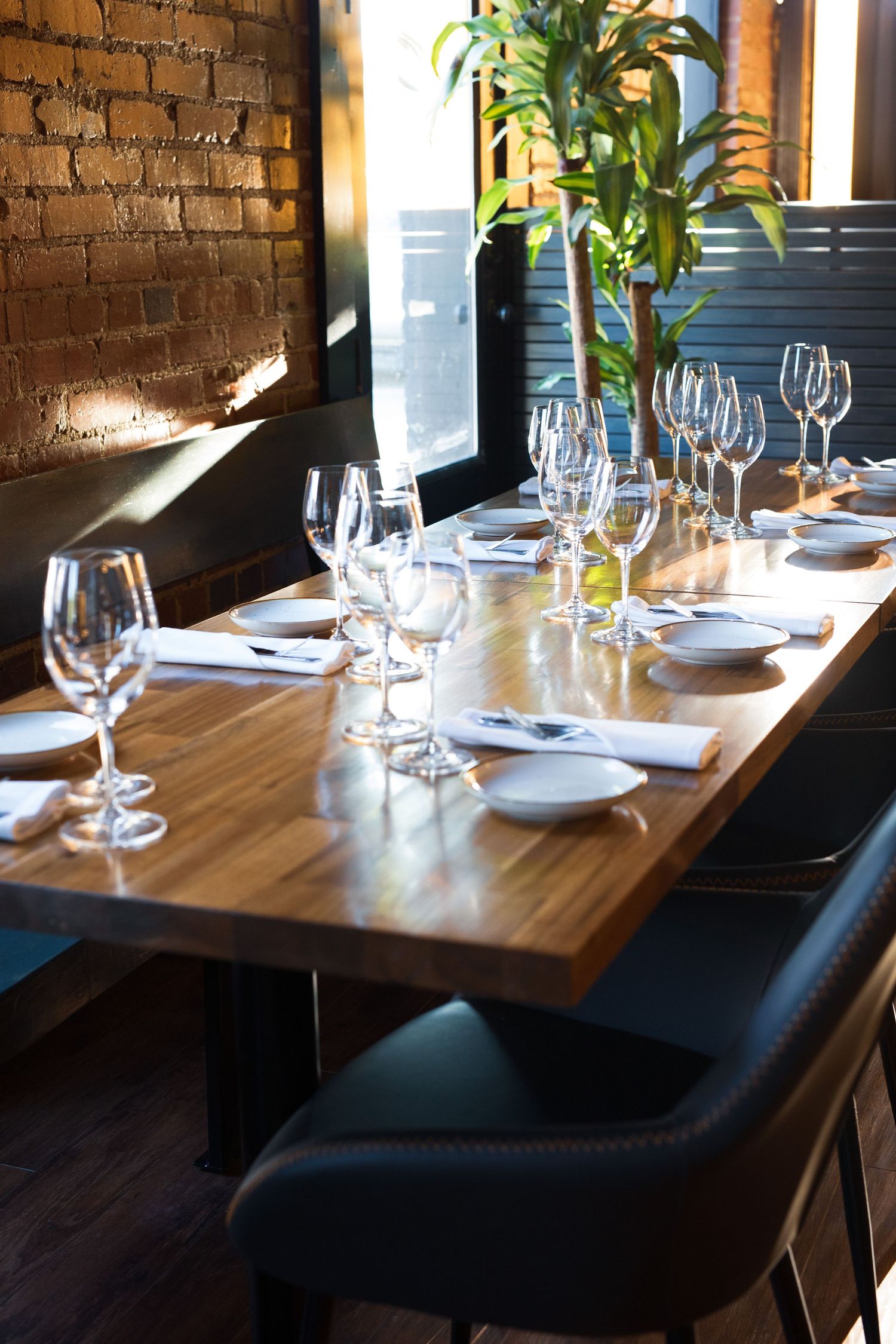 Elegant restaurant table setting with wine glasses and place settings near exposed brick wall in natural light.
