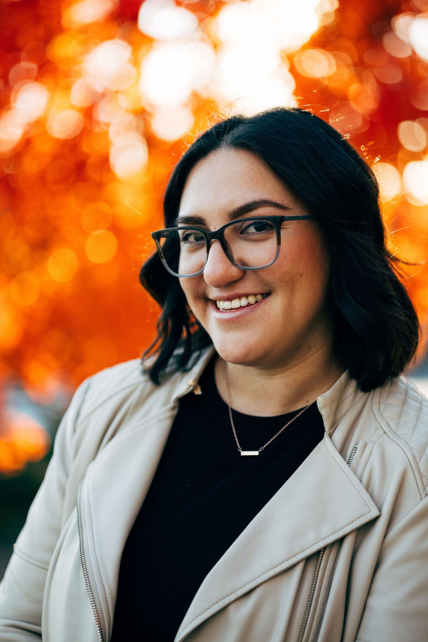 Smiling portrait with autumn bokeh background and beige jacket.