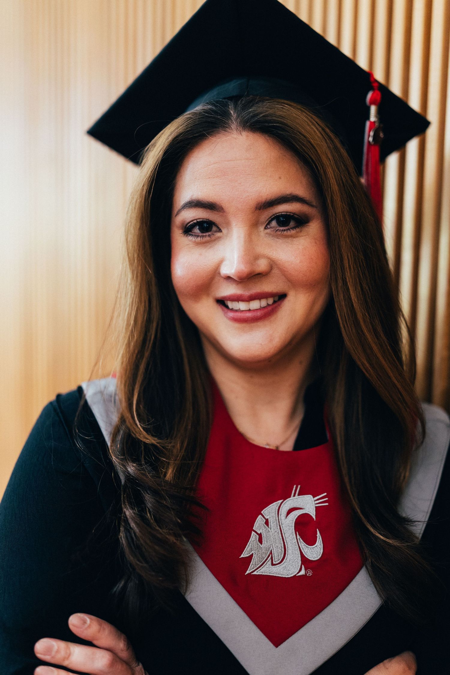 Smiling young woman in graduation cap and gown wearing a Washington State University shirt at her commencement ceremony.
