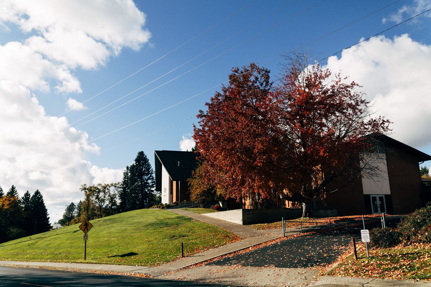 Rolling hills and buildings under puffy white clouds with fall colored trees.