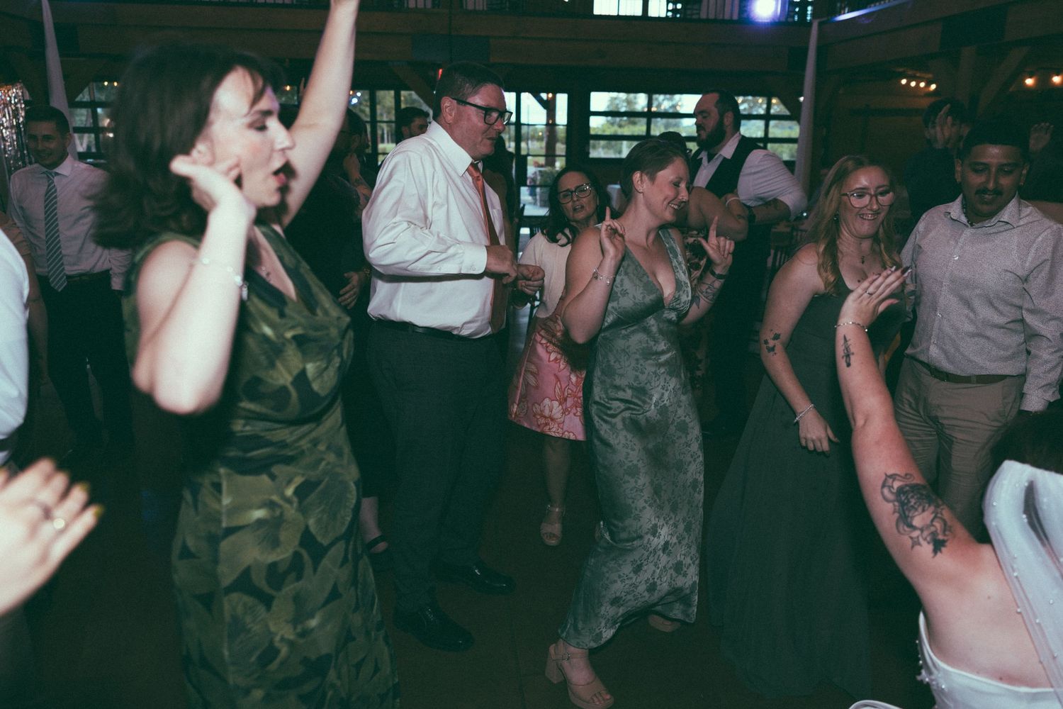 Guests dancing joyfully at a wedding reception, with a woman in a green dress raising her arms in celebration.