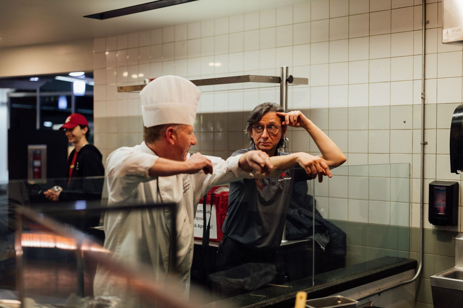 Silhouettes of kitchen workers preparing food behind a counter in a dimly lit restaurant.