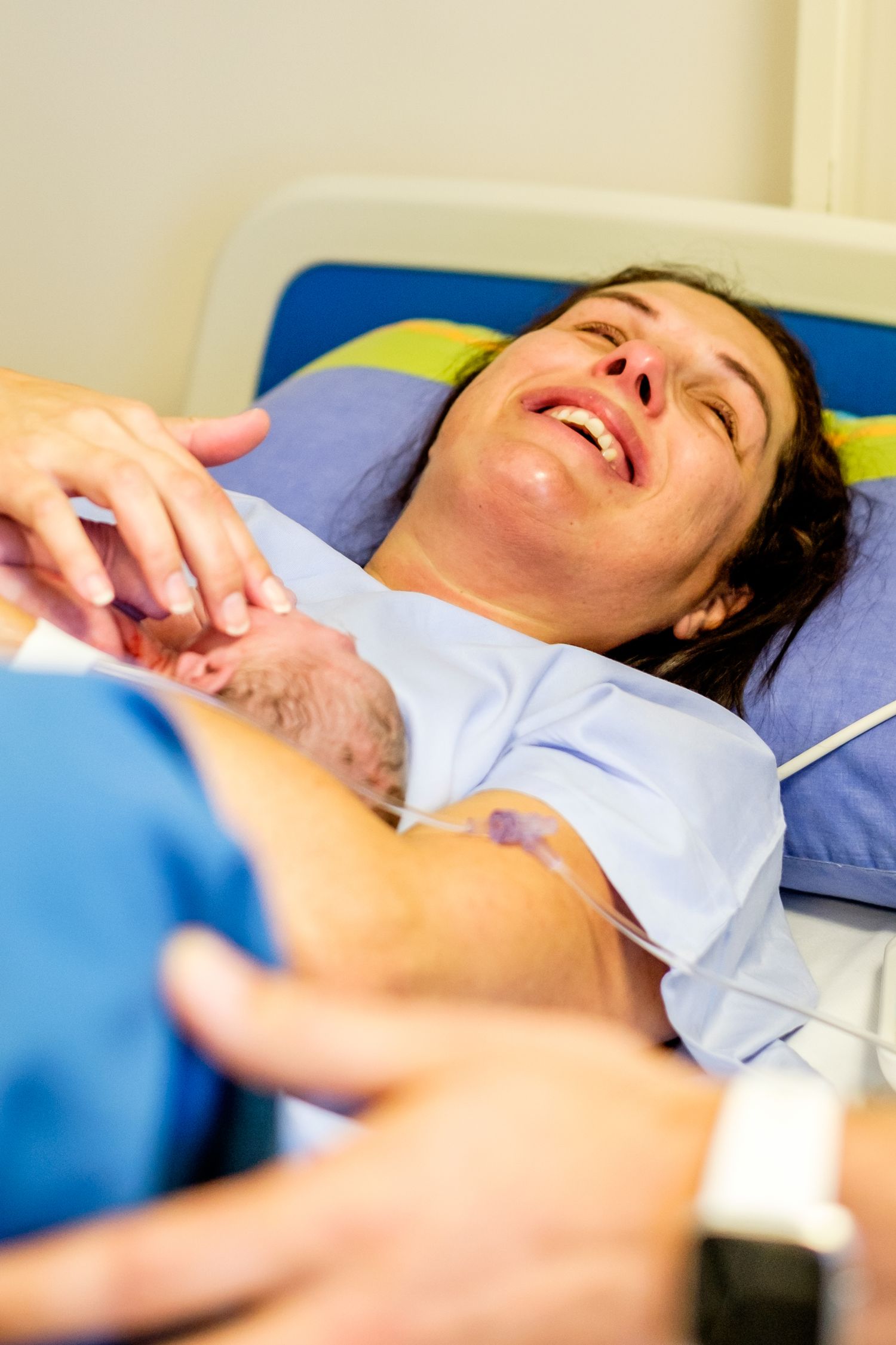 Woman in hospital bed during labor, grimacing in pain while medical staff assists with childbirth delivery.