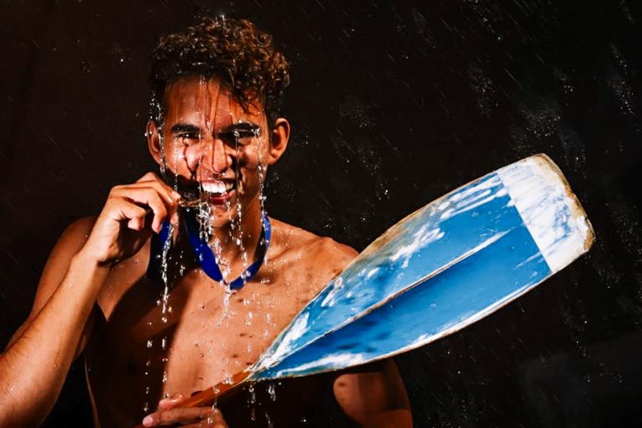 Smiling teen holding a blue paddle with water splashing against a dark background for his teen photoshoot.