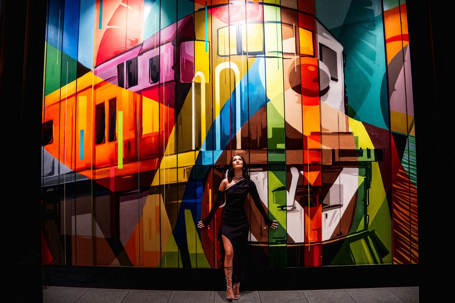 Woman in black dress standing before vibrant colorful urban street mural artwork.