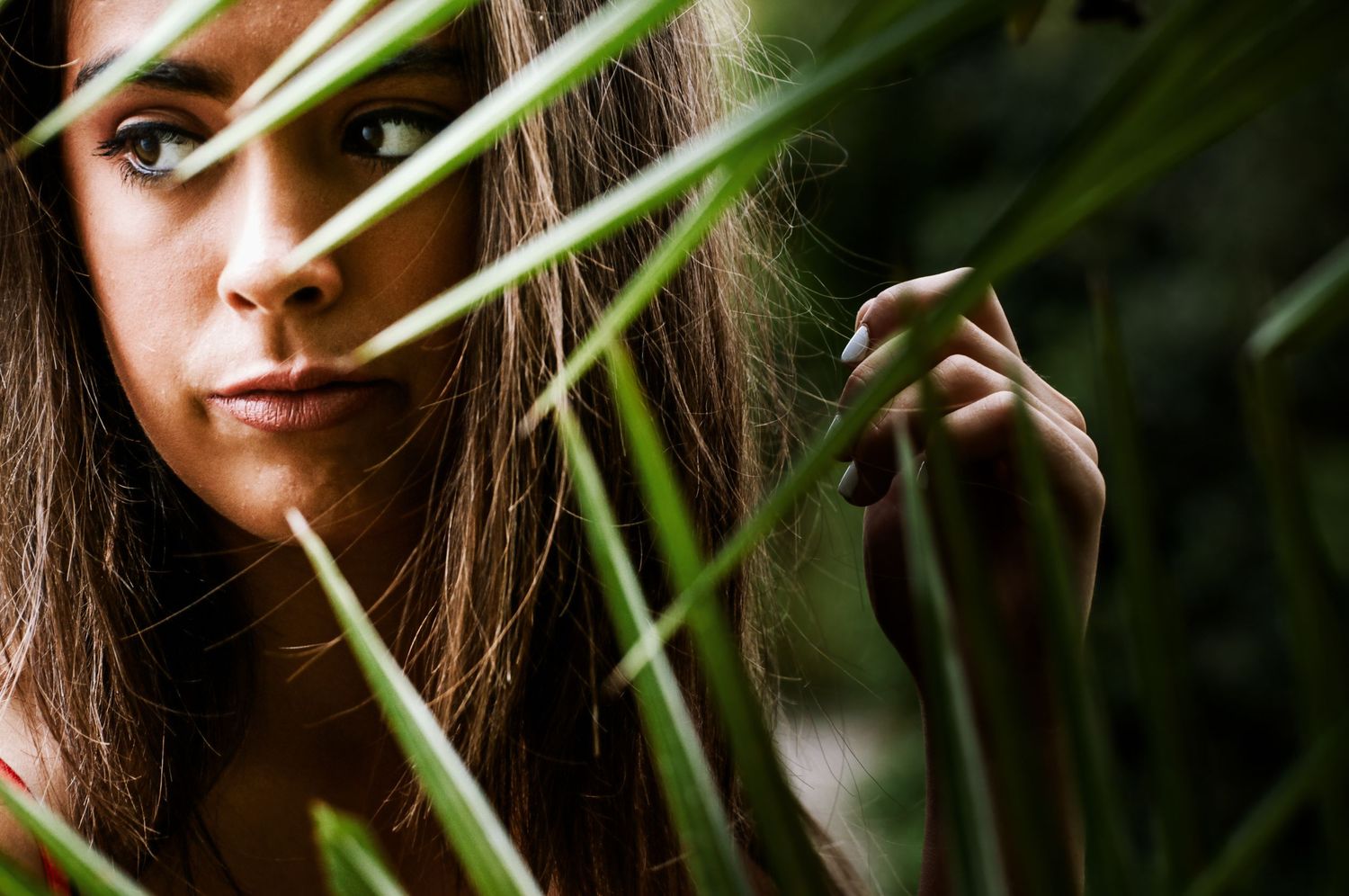 Close-up portrait of a teenager peering through tall green grass blades with intense gaze for her portrait photos.