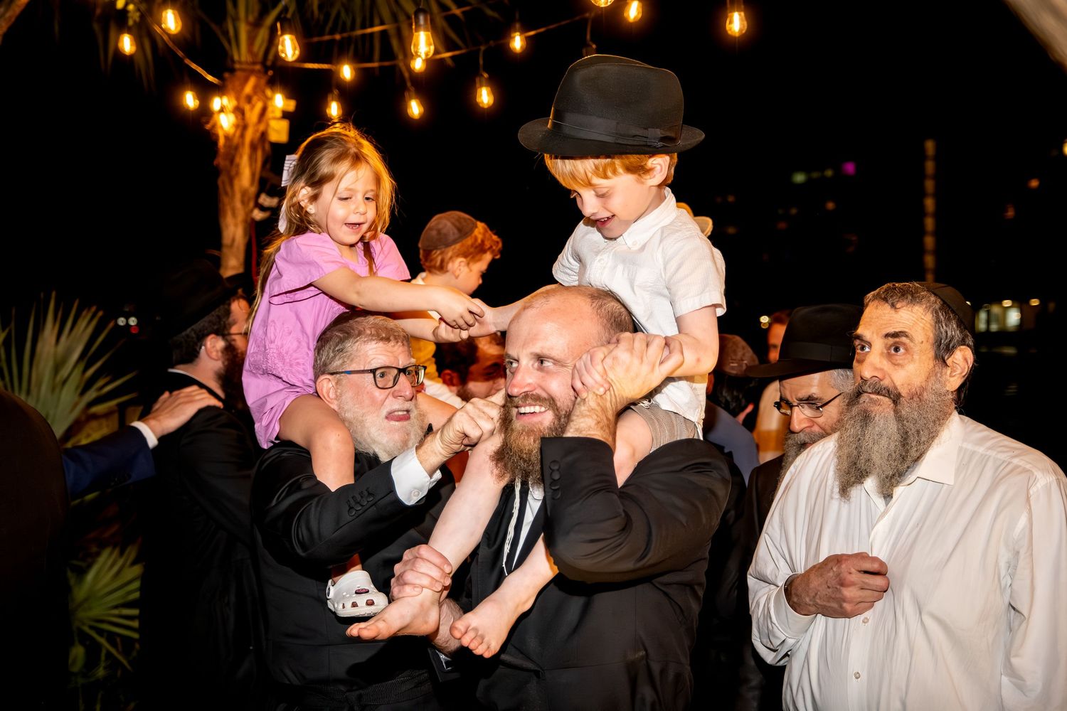Joyful celebration with children lifted on shoulders during an outdoor nighttime party.