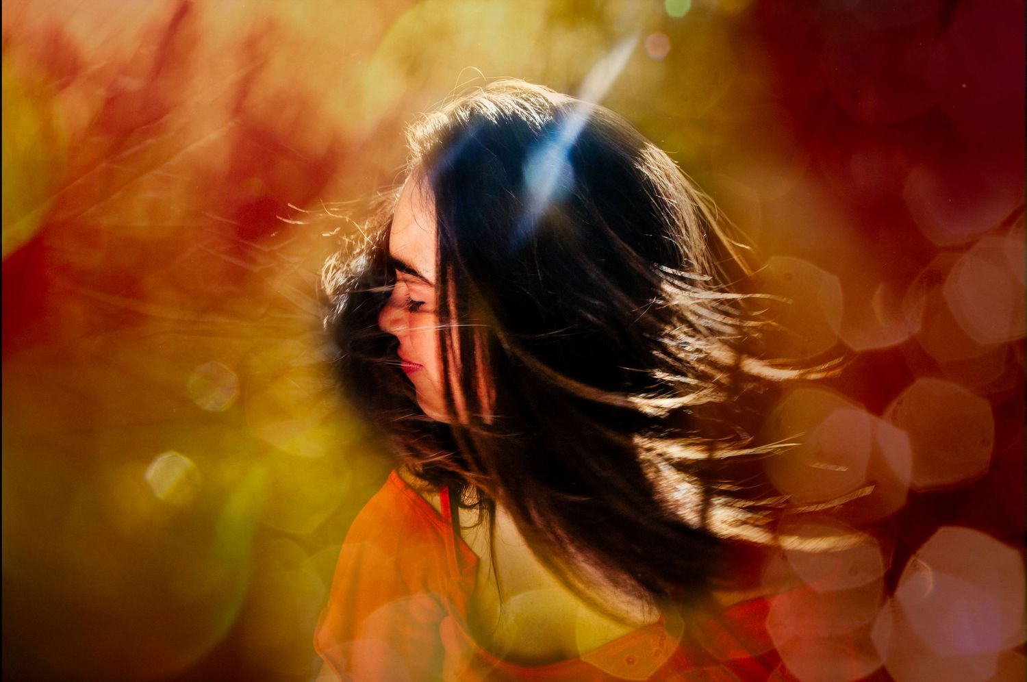 Artistic portrait of a teen girl with hair blowing across face surrounded by warm bokeh lights for a creative teen portrait.