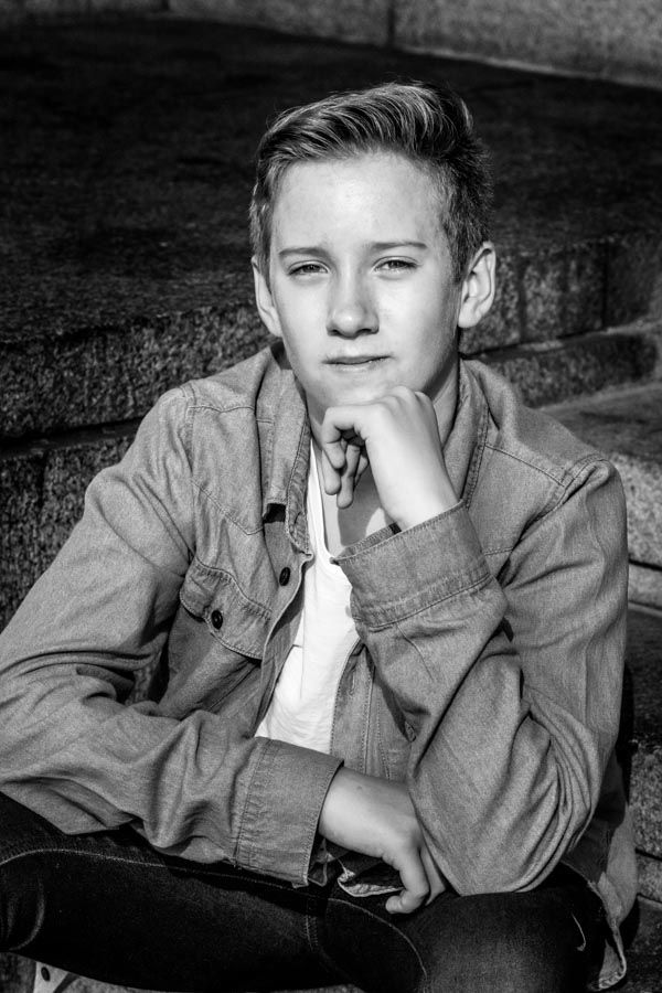 Black and white portrait of a teenage boy sitting thoughtfully on stone steps.