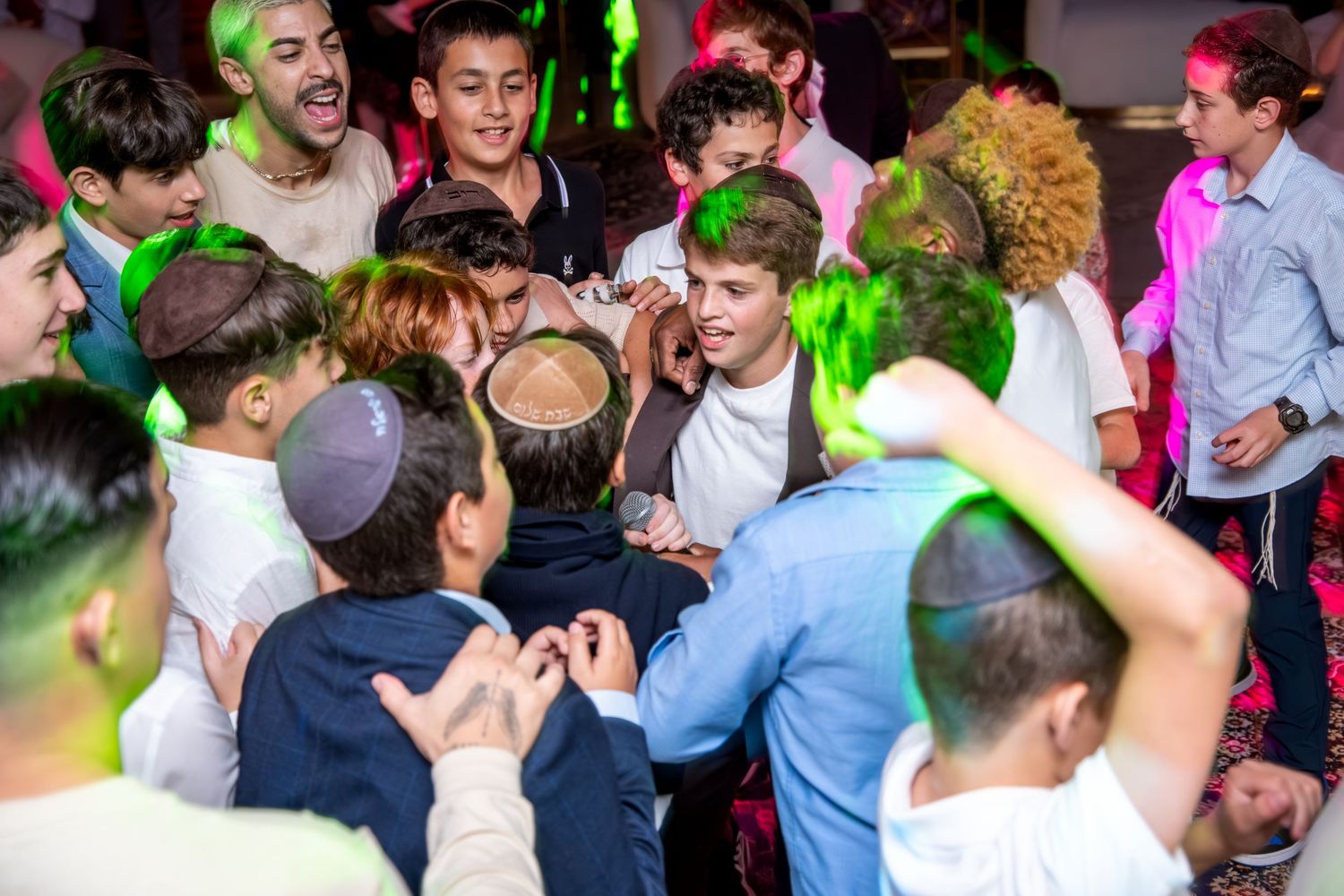 Energetic group of young boys dancing together at a lively celebration with green lights.