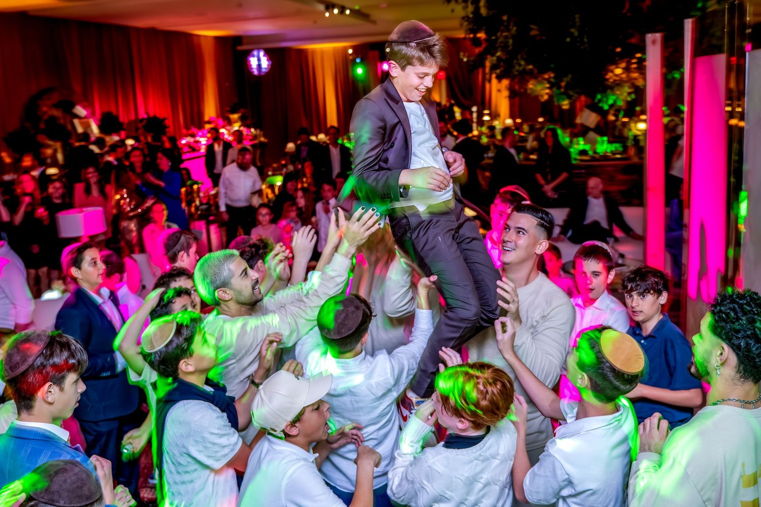 Boy crowd surfing above a group of celebrating kids at a colorful Jewish Bar Mitzvah party.