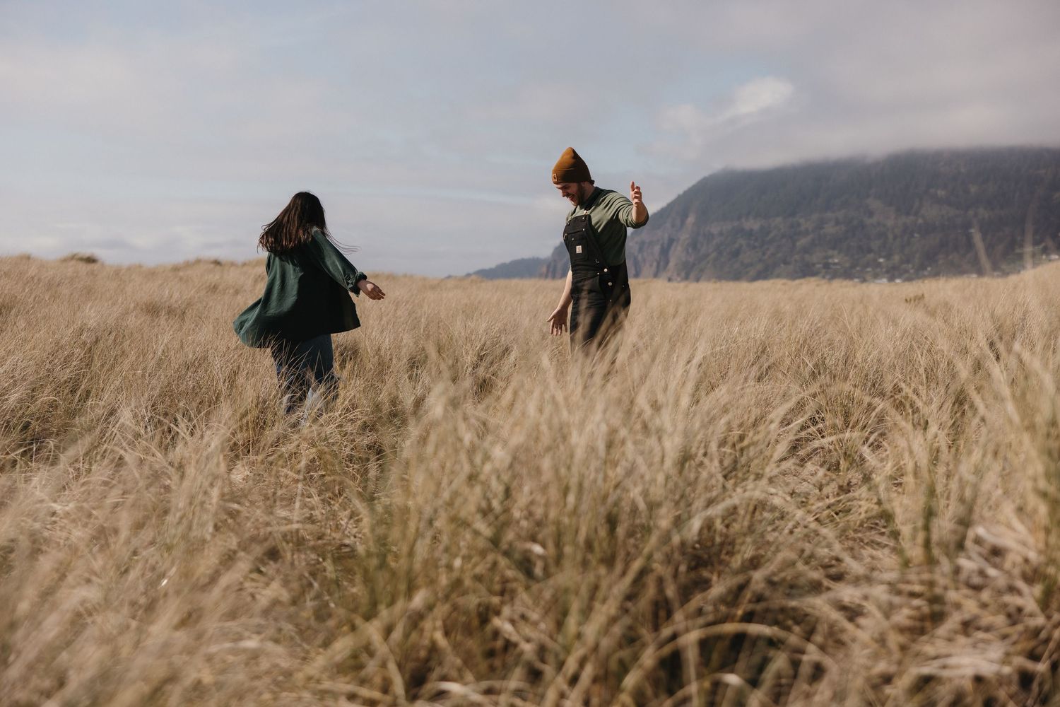 Two adventurous figures walking through tall golden grass in a misty mountain landscape at dusk.