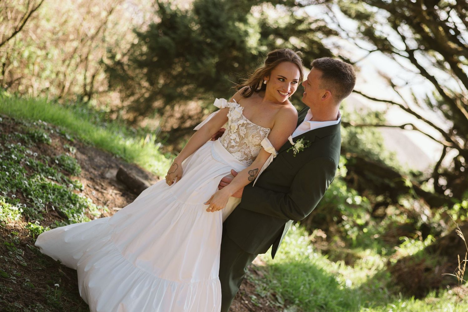 A couple shares an intimate moment outdoors on their wedding day, with the bride wearing a flowing white lace gown.