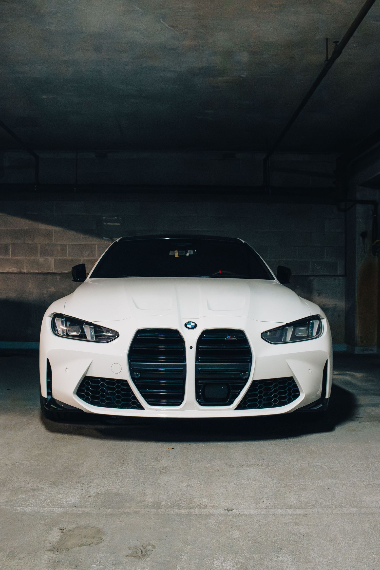 White BMW M4 with distinctive front grille parked in dark garage setting.