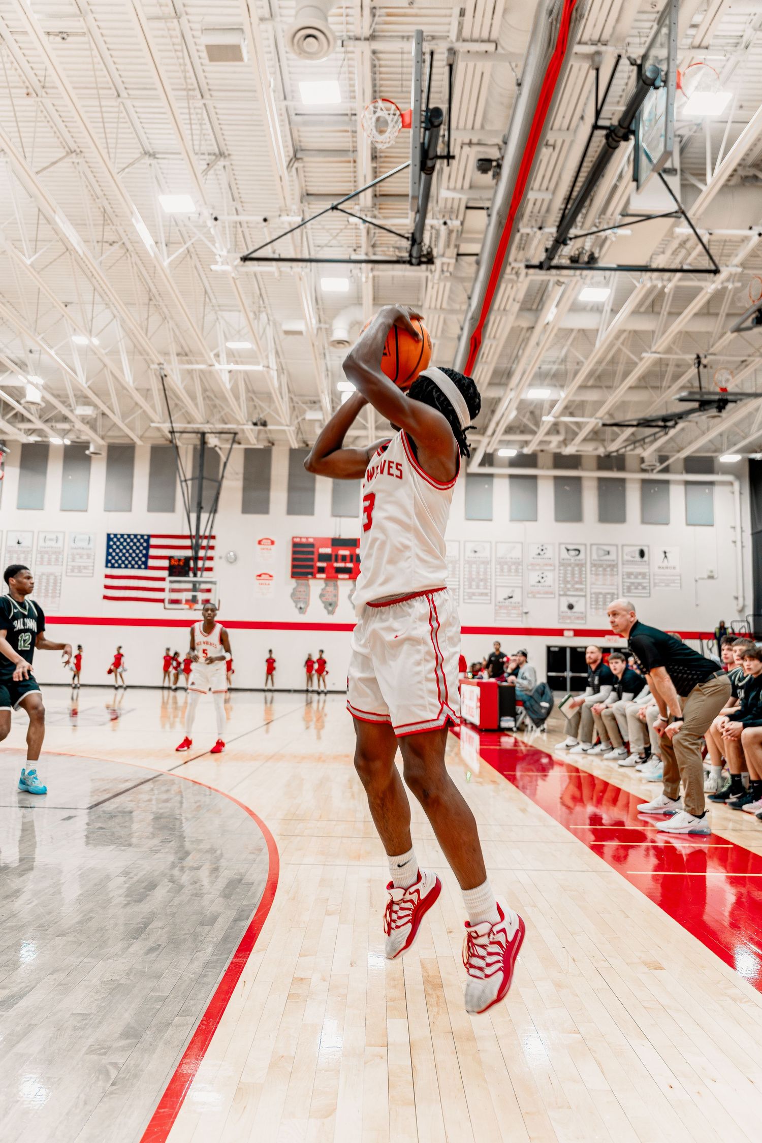 Basketball players practicing drills on a polished court with red and white color scheme.
