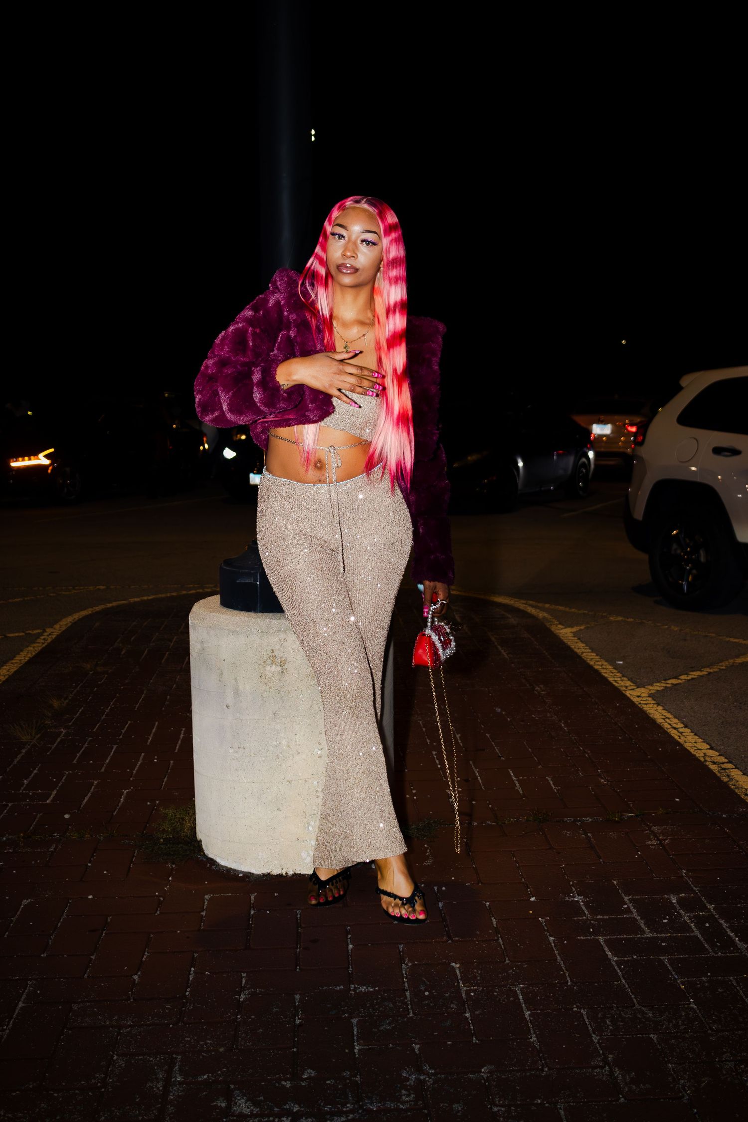 Individual with bright hair strikes dramatic pose in sparkly outfit outdoors.