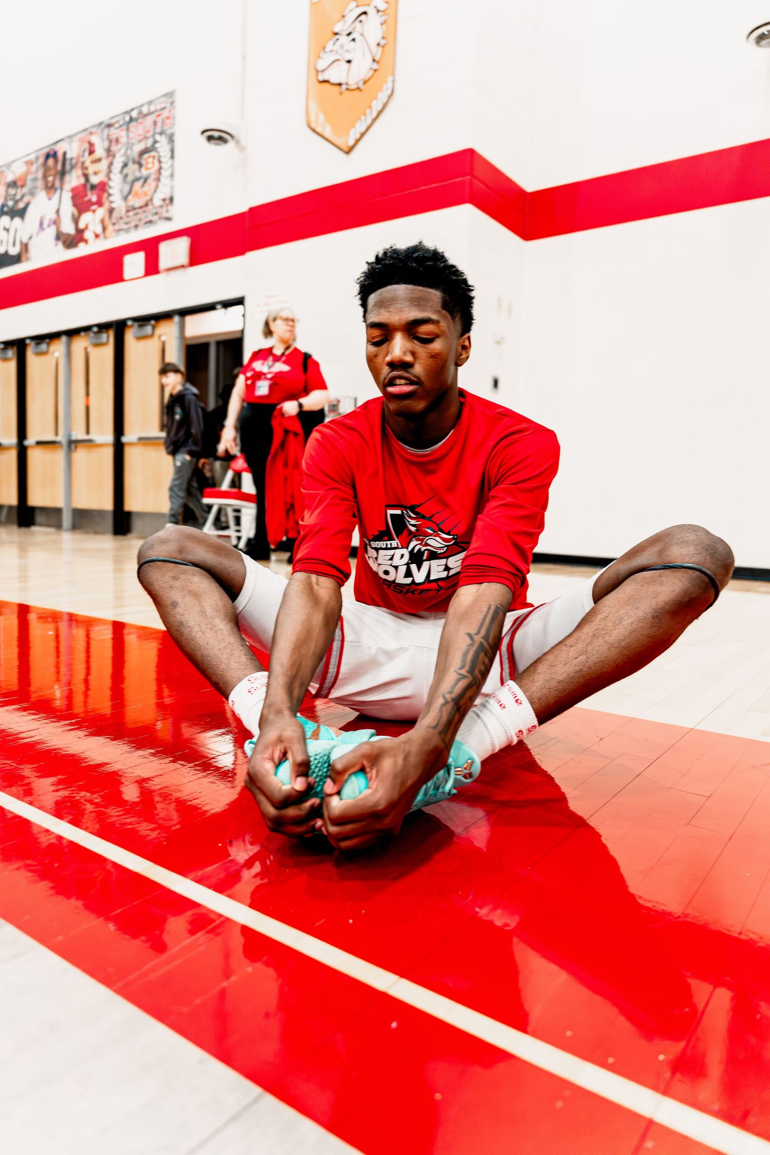 Athlete performs stretching exercises on a red mat in a training facility with white walls.
