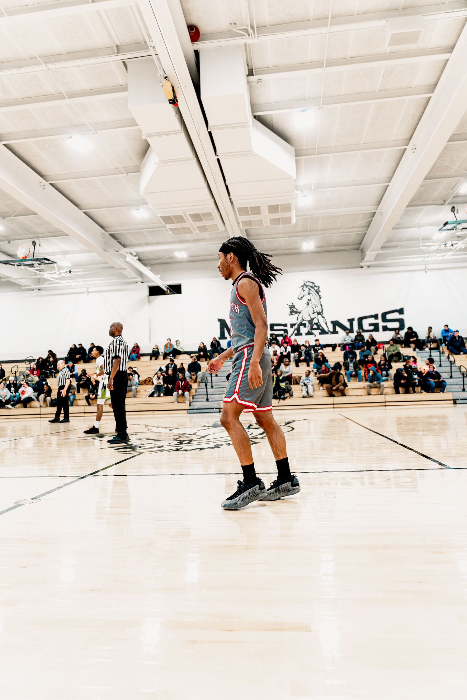 Basketball player in blue uniform dribbles on indoor court during game with spectators in gymnasium bleachers.