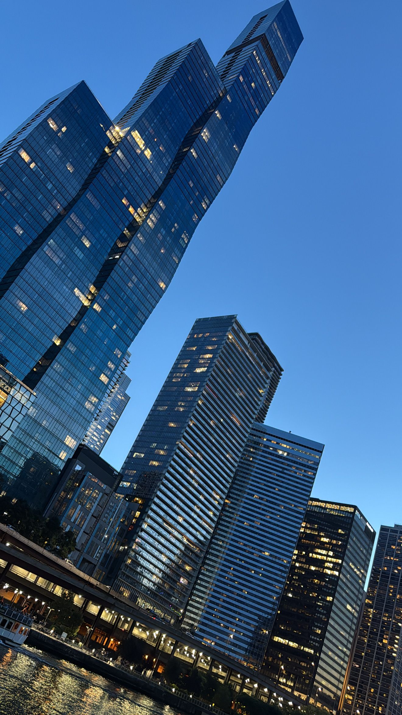 Modern glass skyscrapers reflect evening light against a deep blue sky in an urban cityscape.