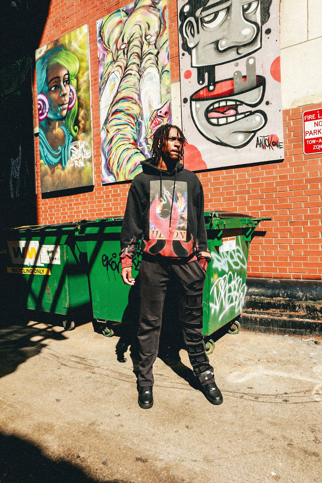 A figure stands against a brick wall decorated with colorful graffiti art and green benches in an urban setting.