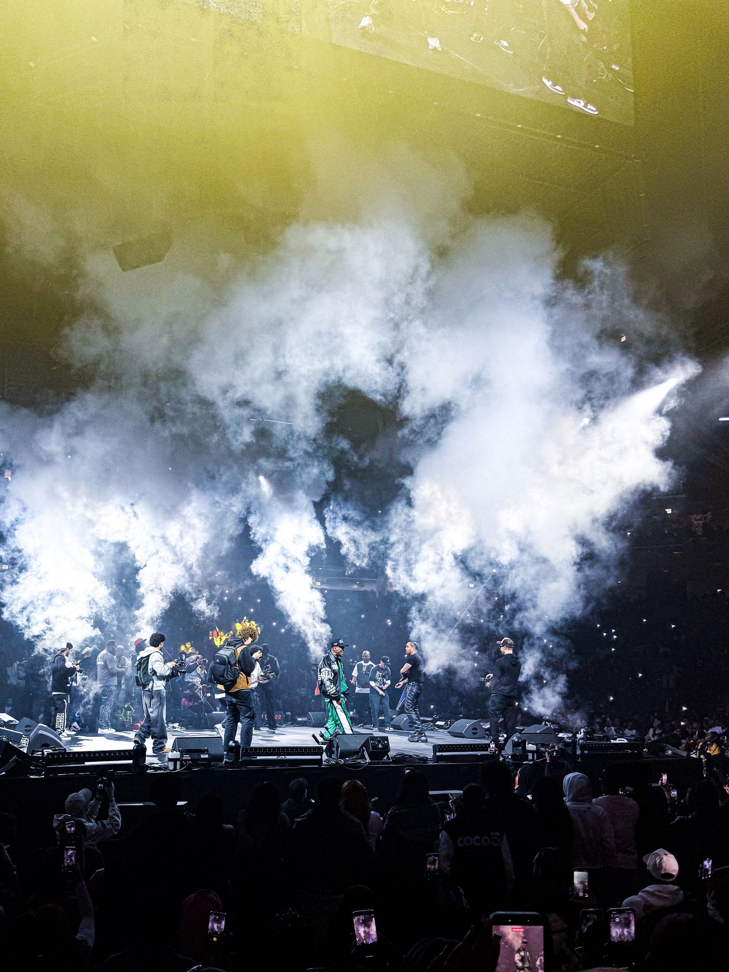 Concert performers on stage surrounded by dramatic white smoke effects and lighting during a live performance.
