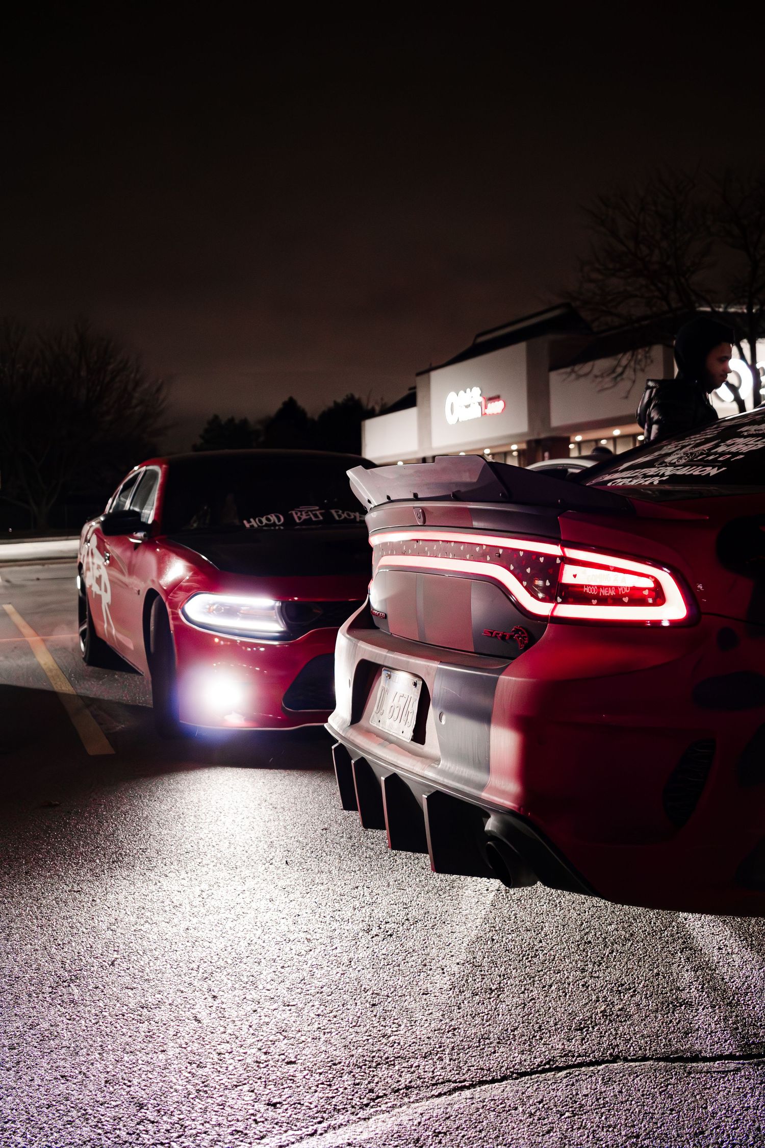 Line of sports cars with glowing red tail lights in dark parking lot.