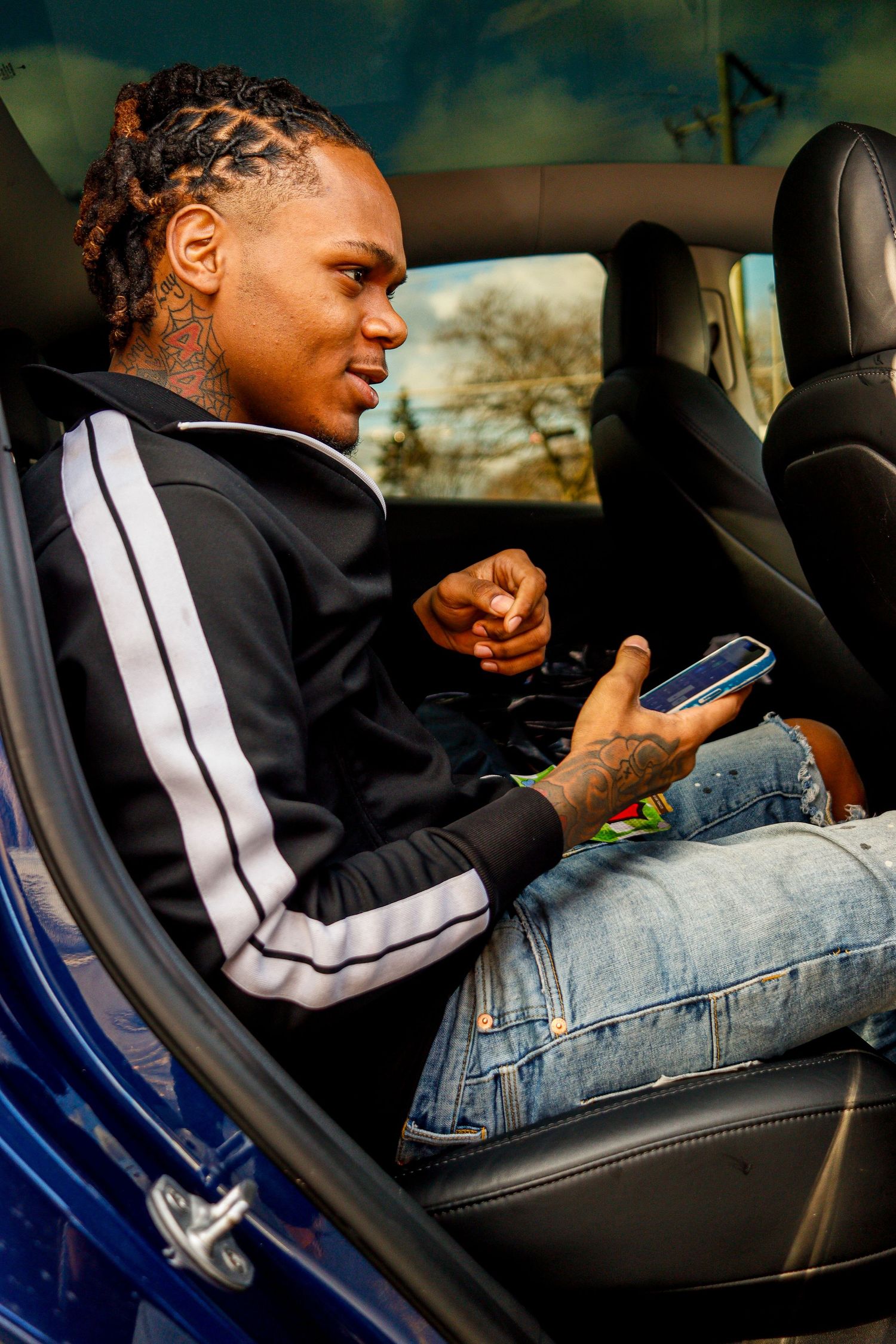A person wearing a black and white jacket sits in a car seat while looking at their phone.