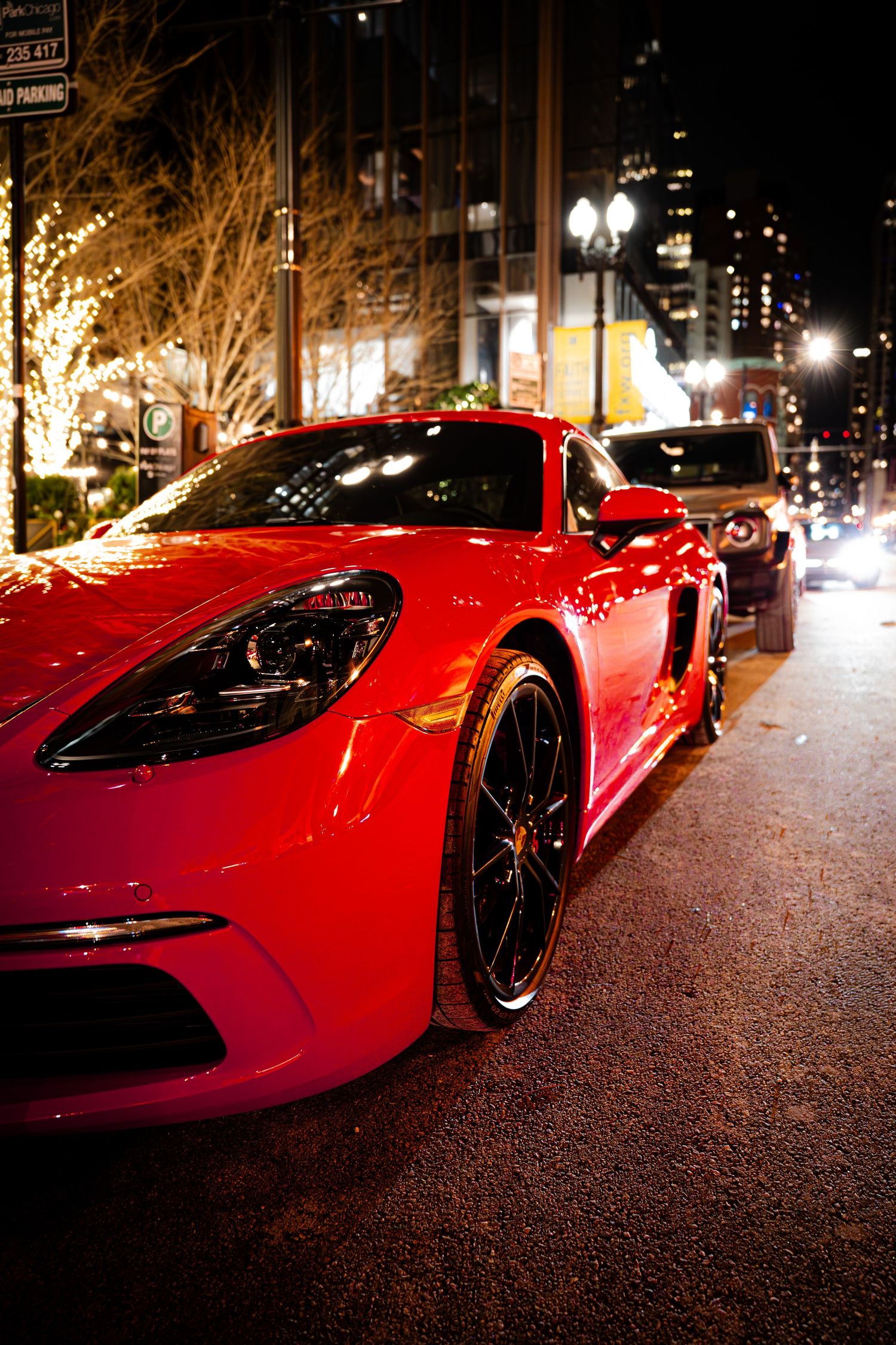 Red Porsche sports car parked on city street at night with illuminated trees.