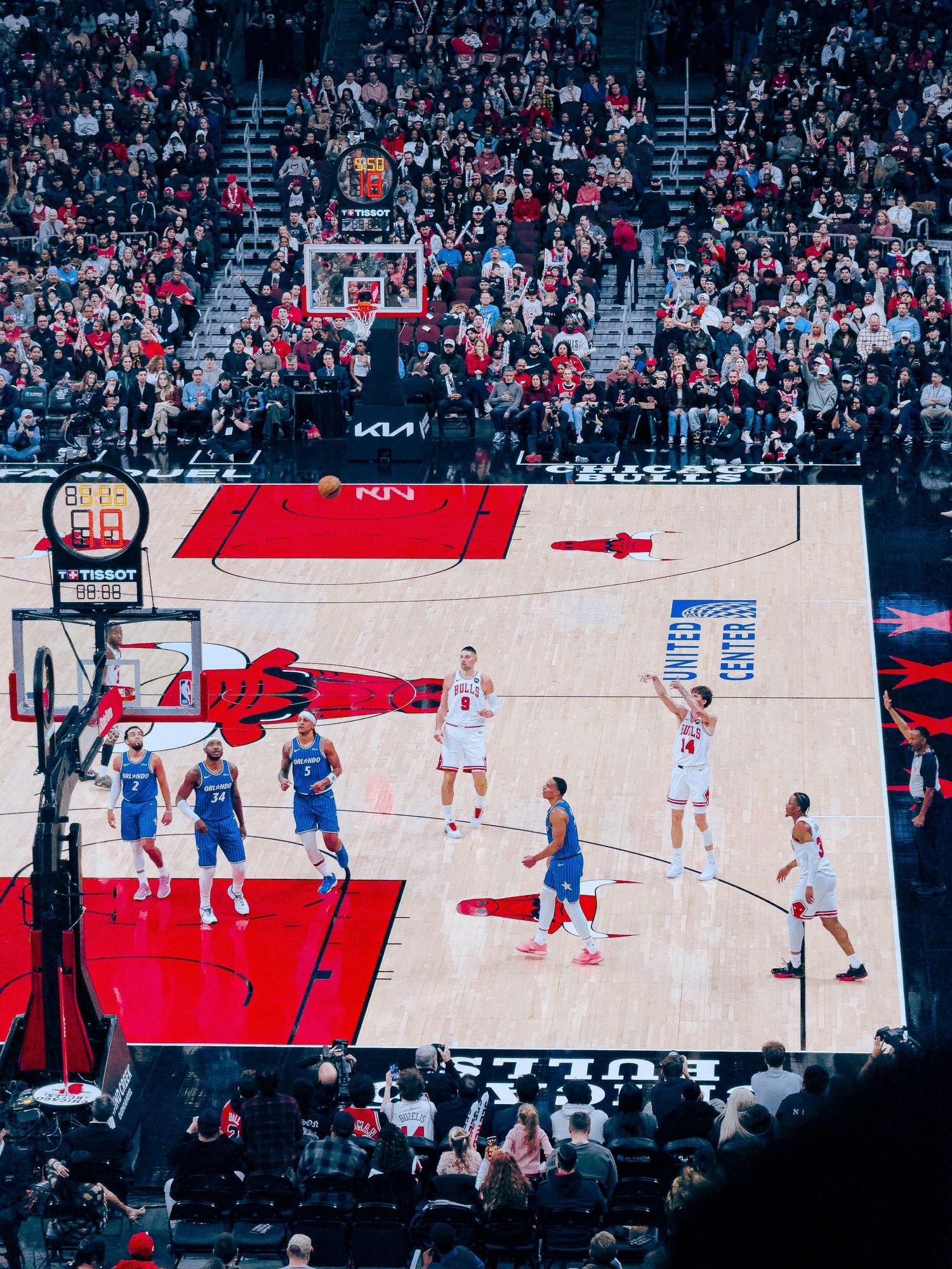 A basketball game in progress on a red and white court viewed from an elevated angle showing multiple players in action.