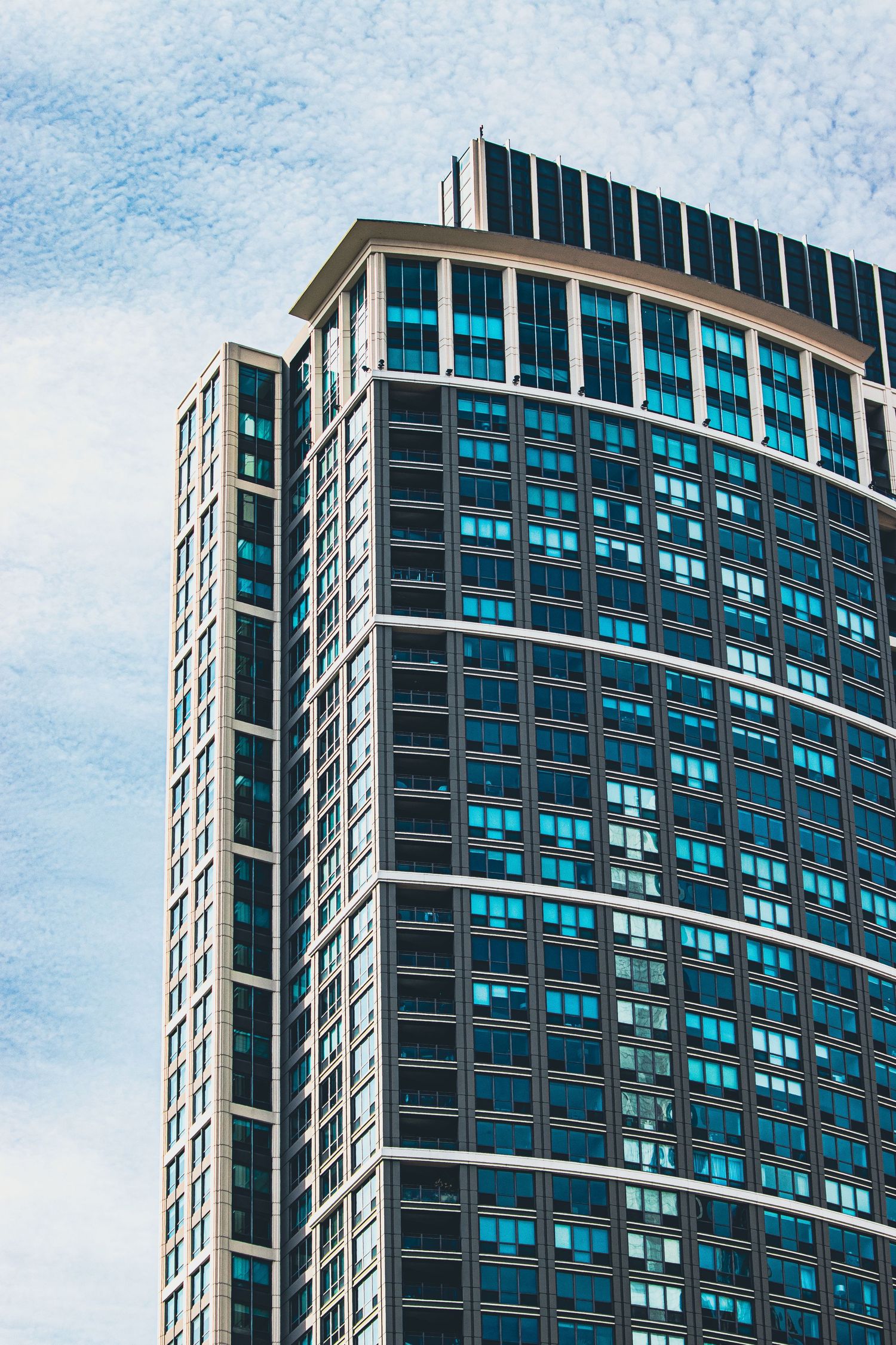 Modern glass and steel high-rise building with curved facade and blue-tinted windows against cloudy sky.