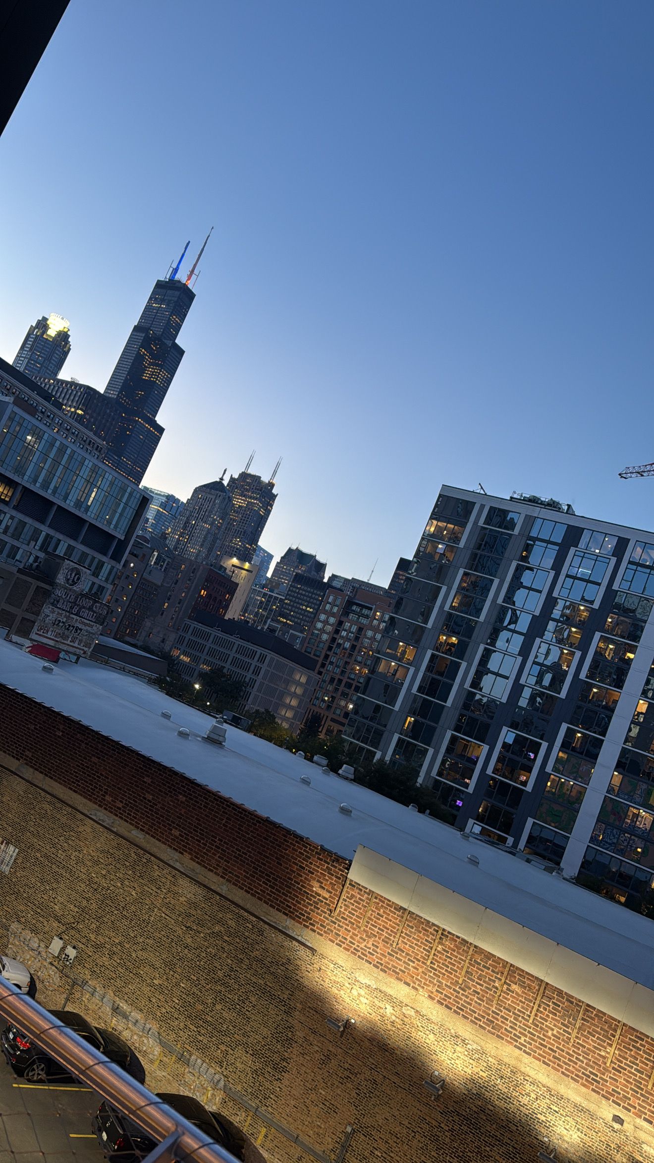 Chicago skyline at dusk with illuminated brick wall in foreground against deep blue sky.