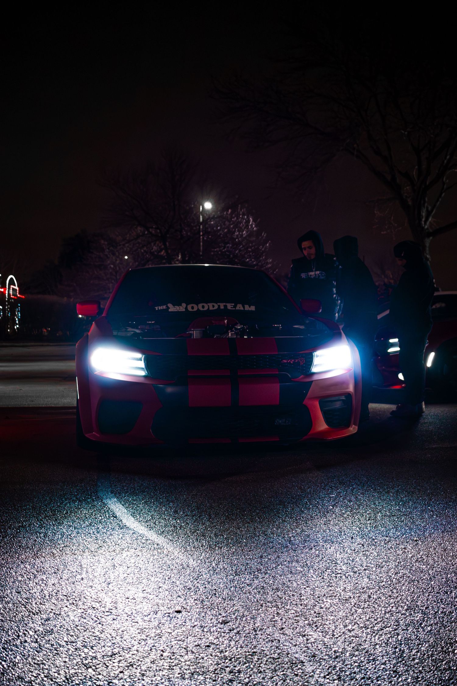 Row of cars with bright headlights illuminating dark parking lot at night.