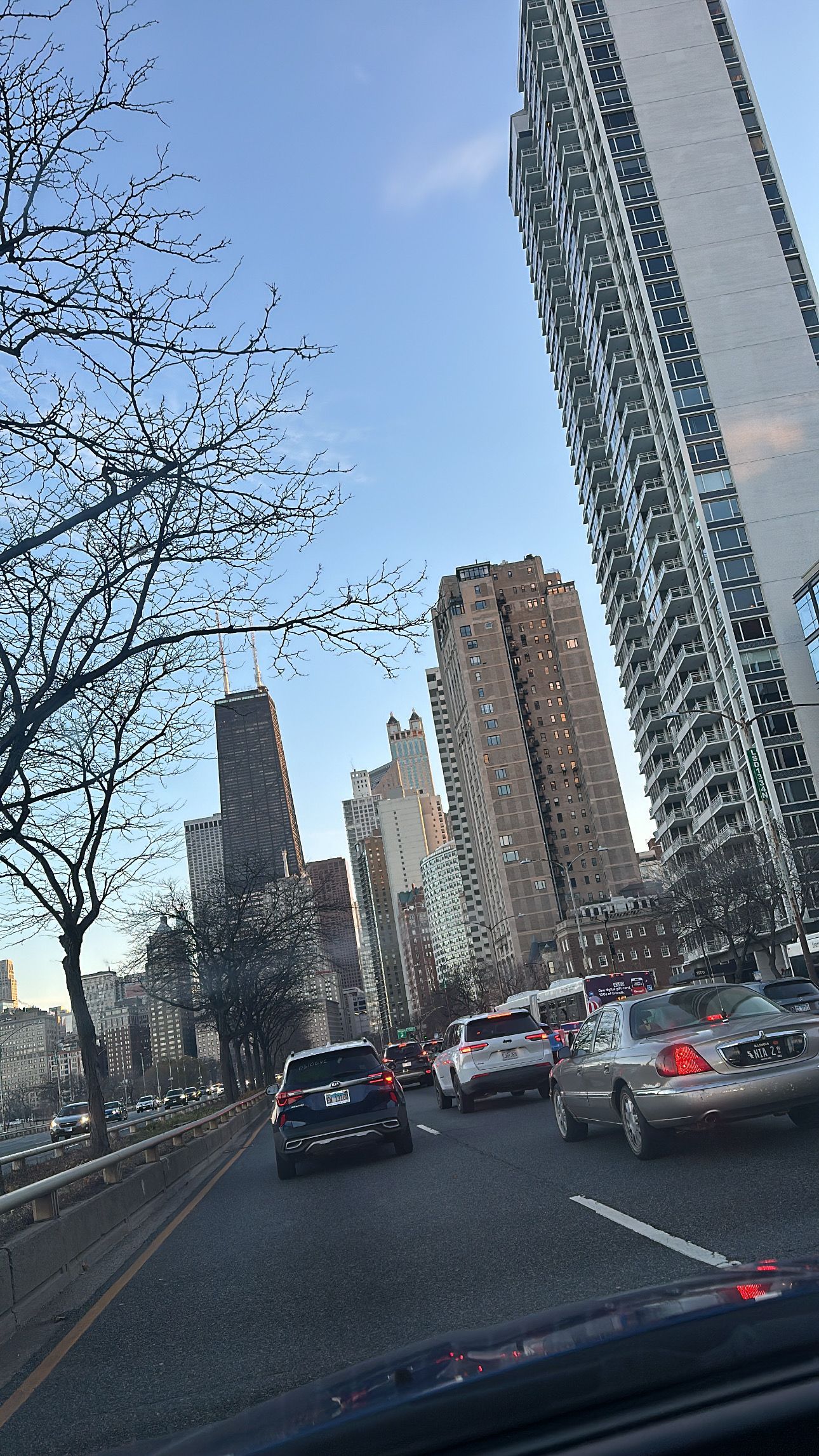 Traffic and tall residential buildings line the street on a cloudy day in an urban setting.