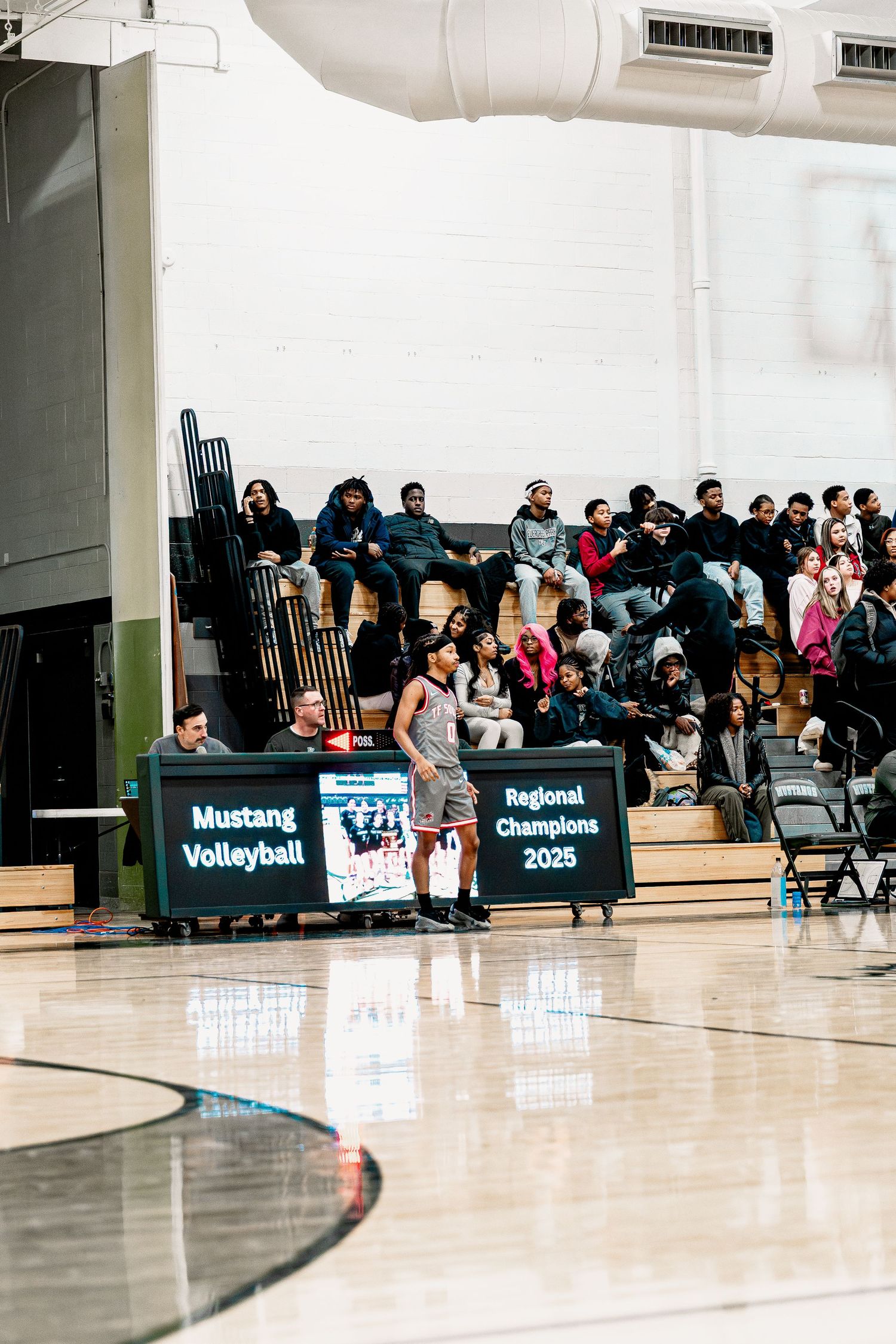 A crowded gymnasium with spectators seated on folding chairs watching a volleyball game with black banners on display.