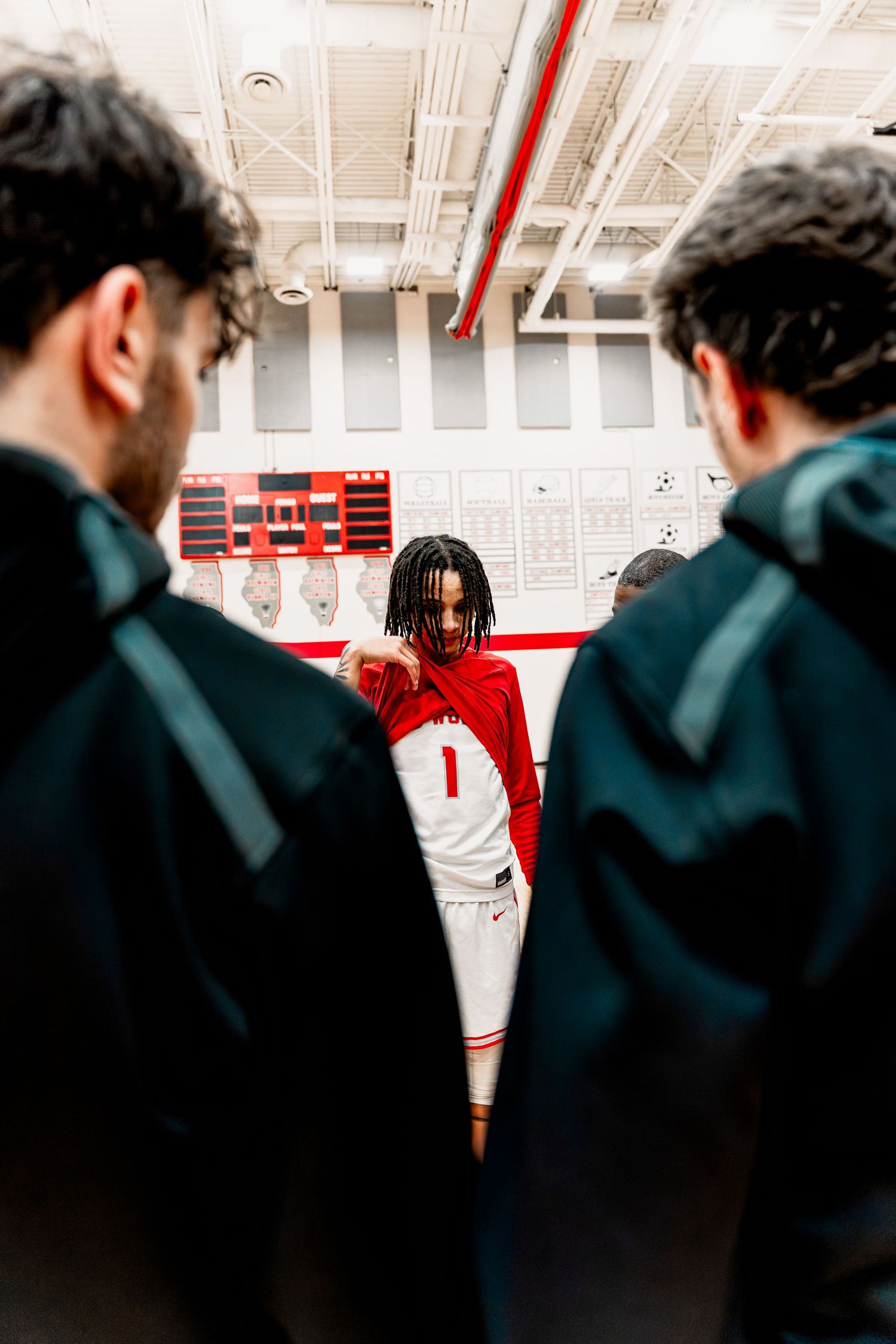 Basketball player in red jersey practicing dribbling drills in a gymnasium with spectators watching.
