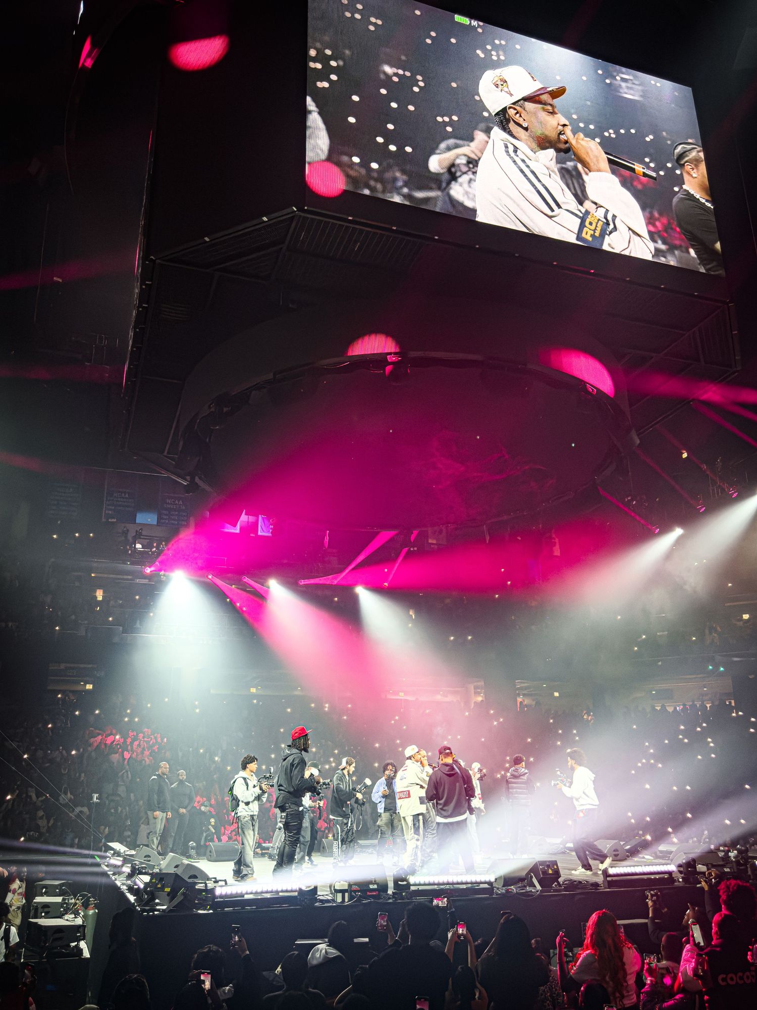 Concert stage illuminated with dramatic pink and white spotlights creating an atmospheric performance environment.