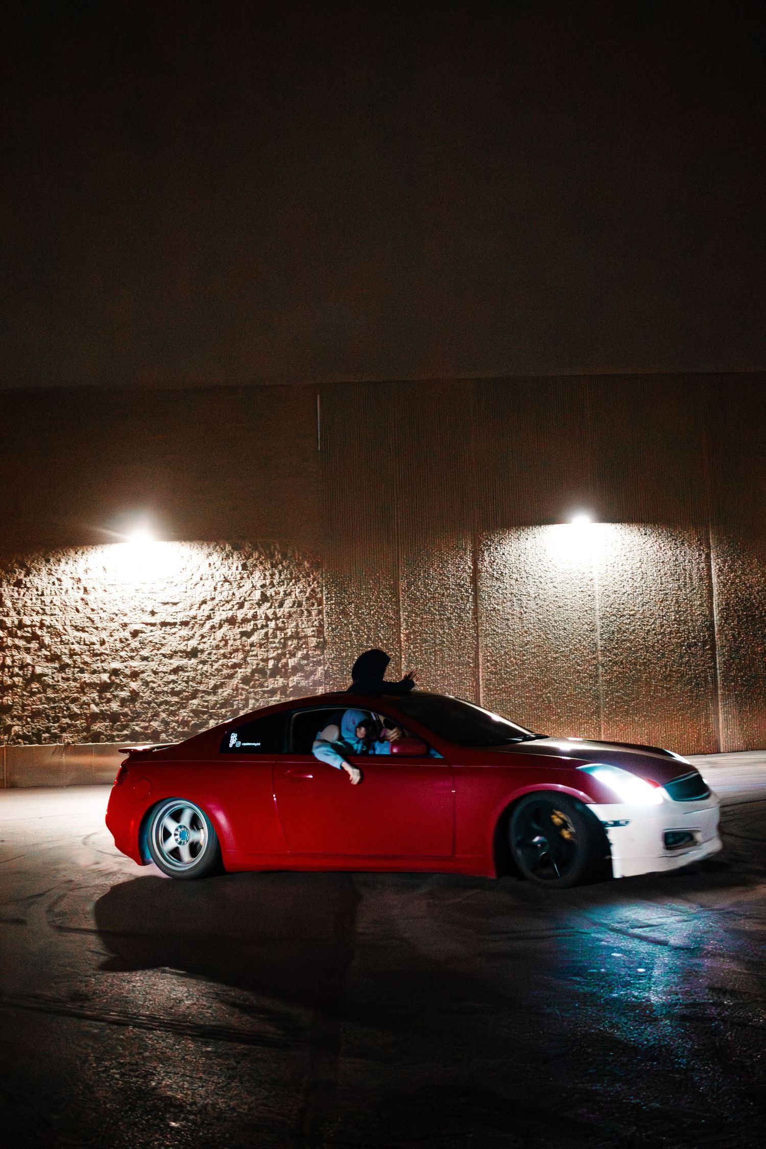 Red sports car illuminated by overhead lights in dark parking garage.