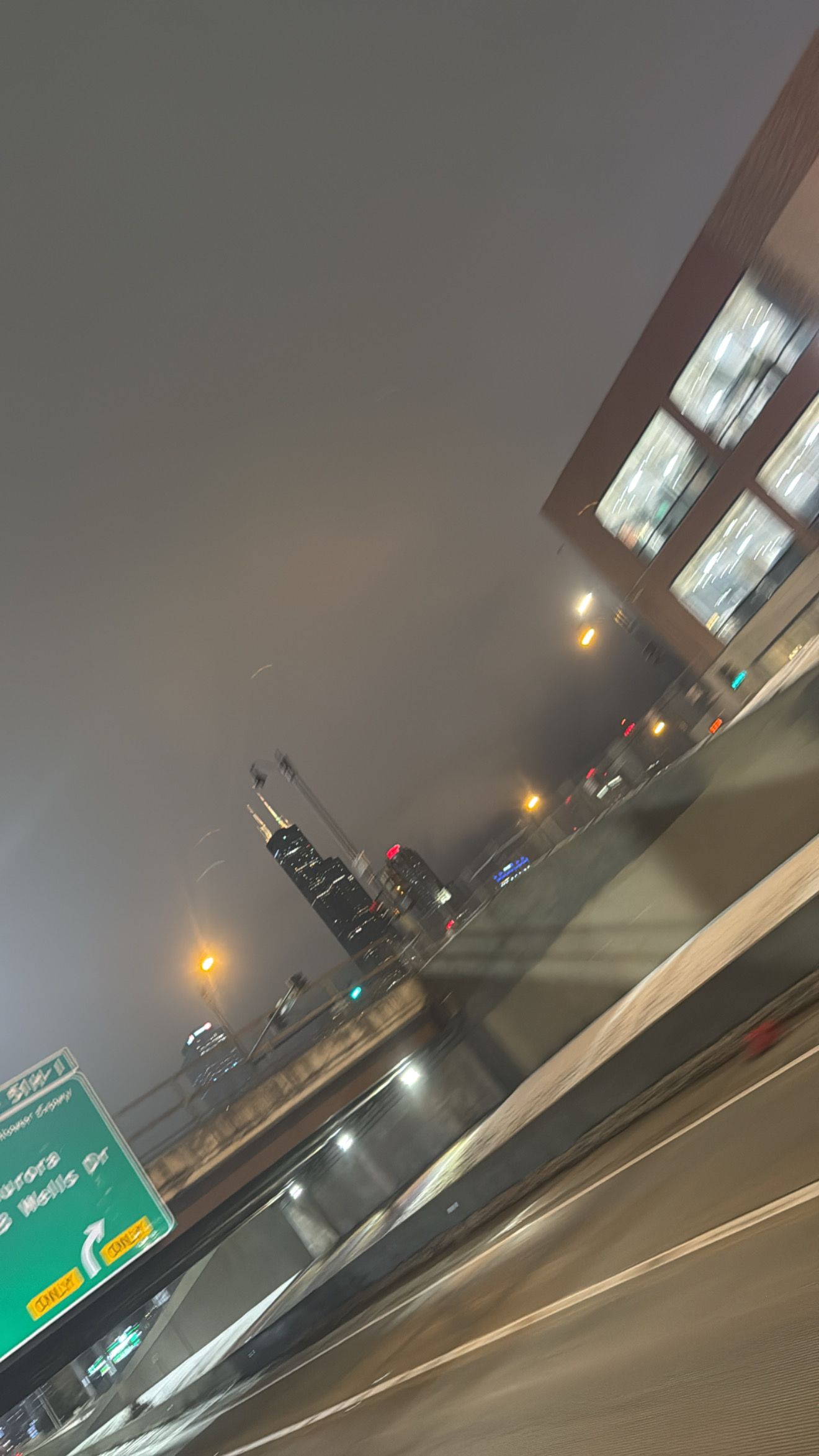 A blurry nighttime highway scene with street lights and road signs visible through a car window.