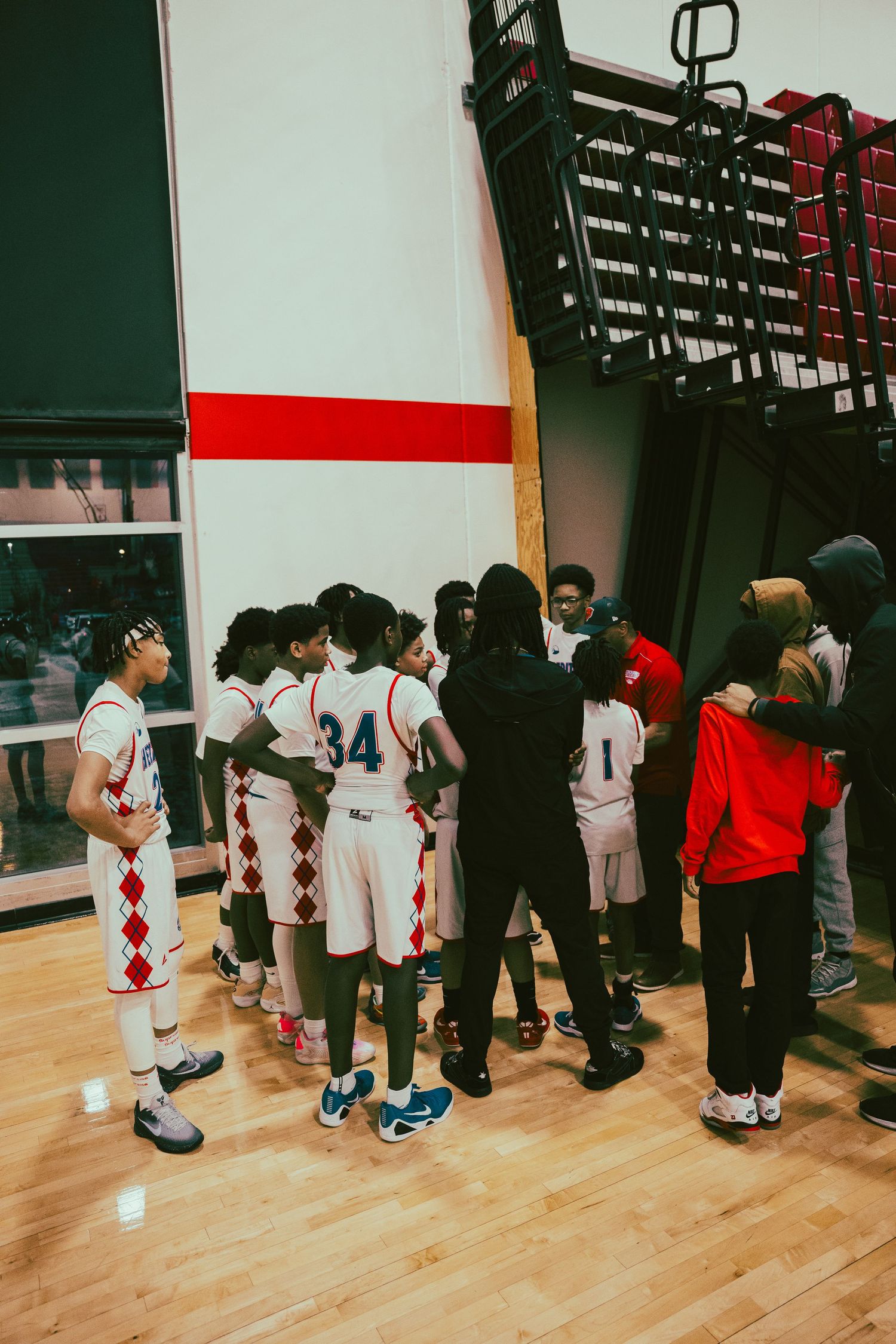 Basketball players in white uniforms line up against a wall during a team gathering in an indoor gymnasium.