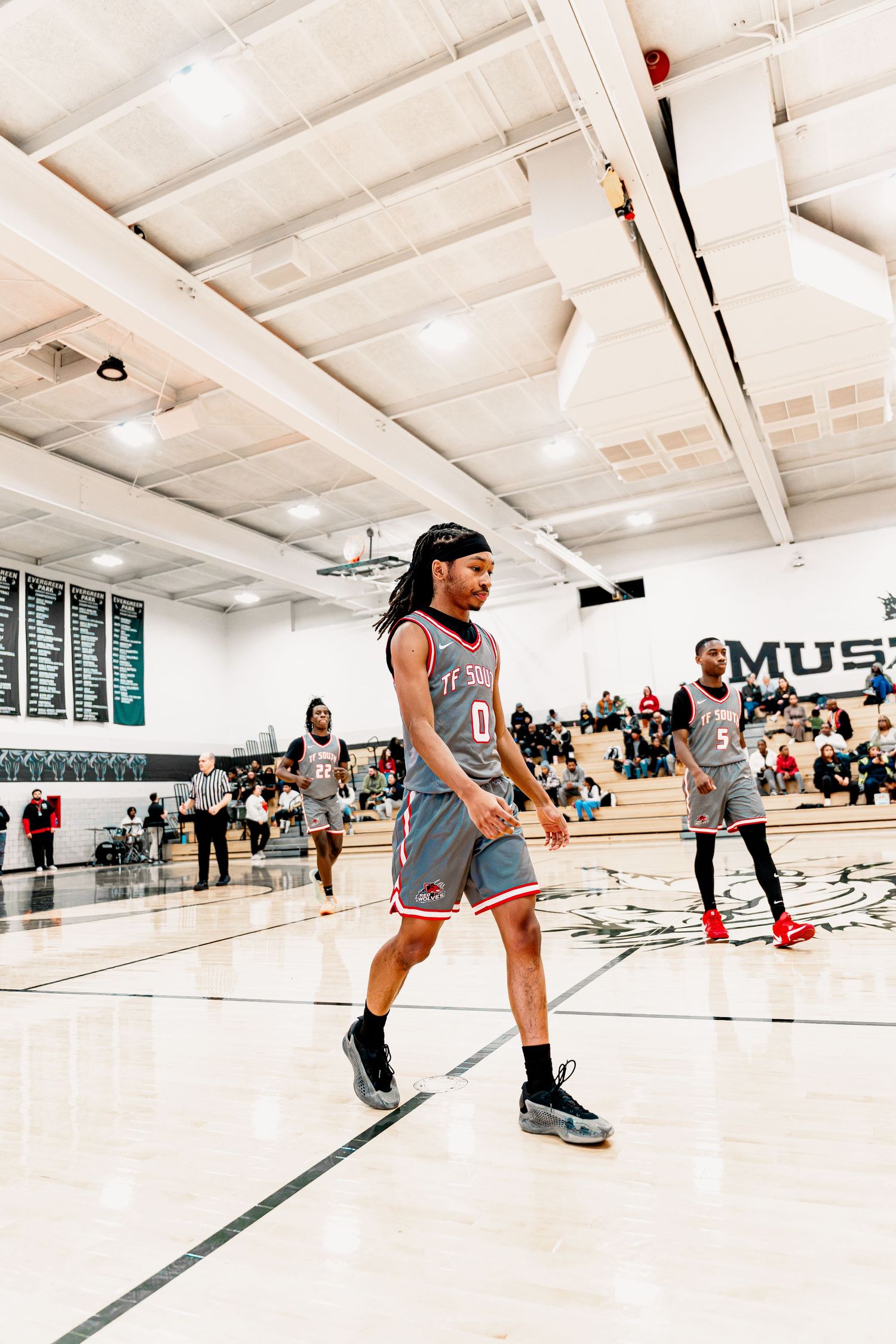 Athletes practice drills on a bright indoor basketball court with spectators watching from the sidelines.