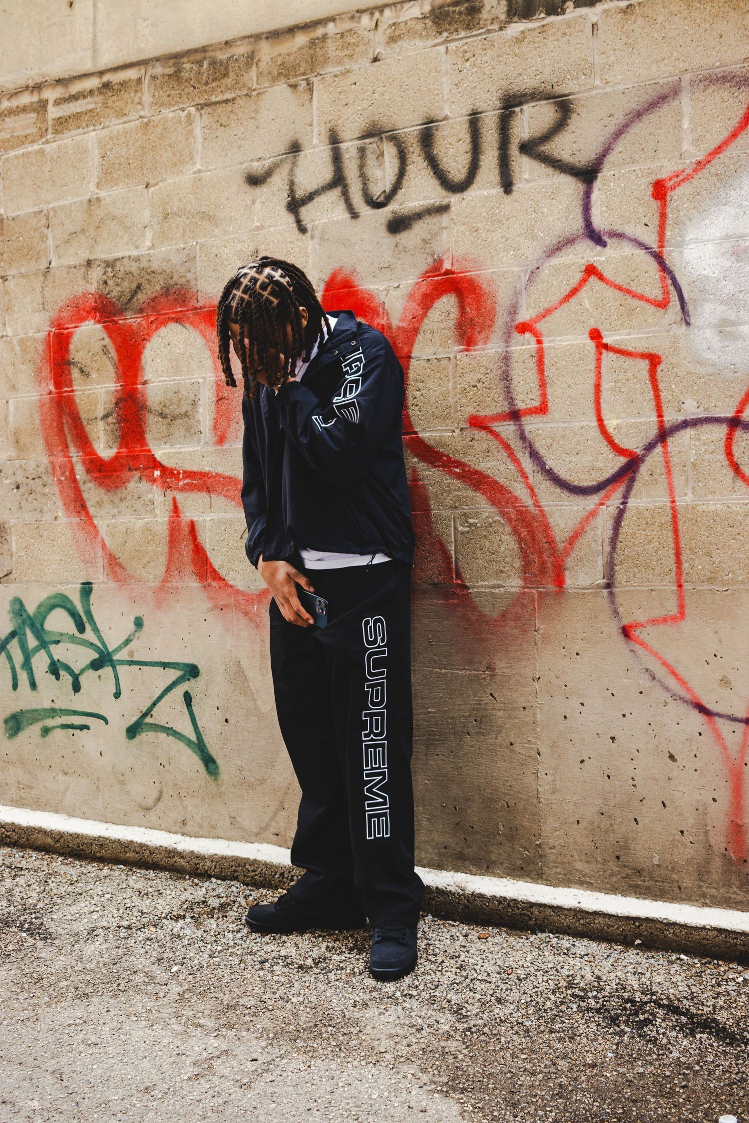 Person in dark clothing standing against graffiti-covered concrete wall.