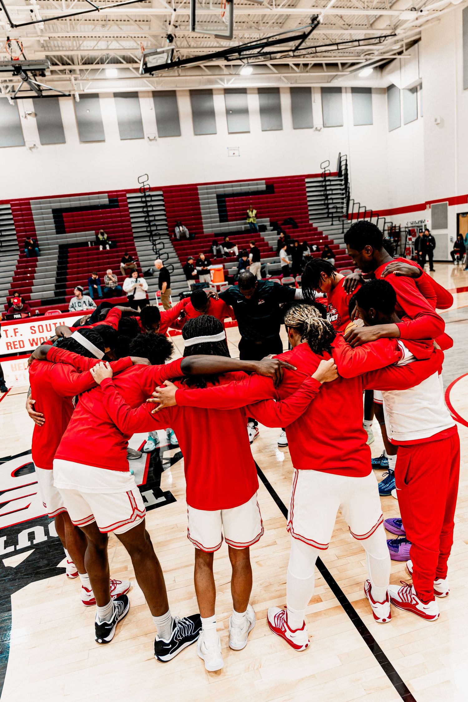 A group wearing red jackets performs a synchronized dance routine in a gymnasium with red and white walls.