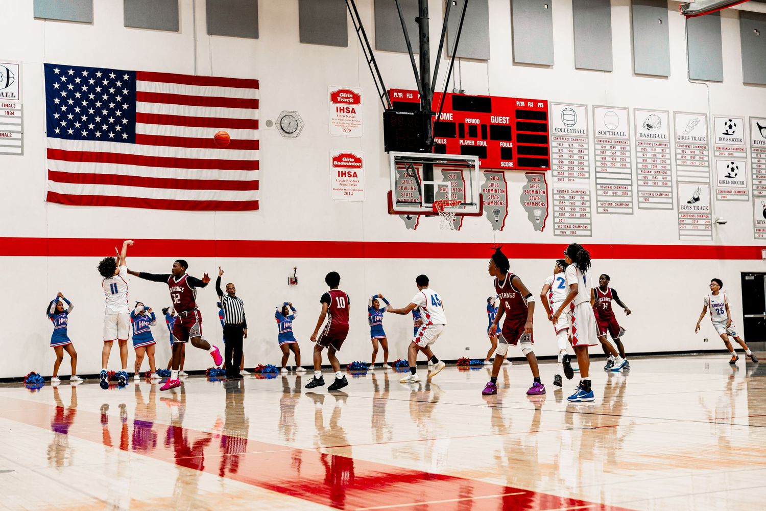 Basketball players compete on a court with American flags displayed on the wall during an indoor game.