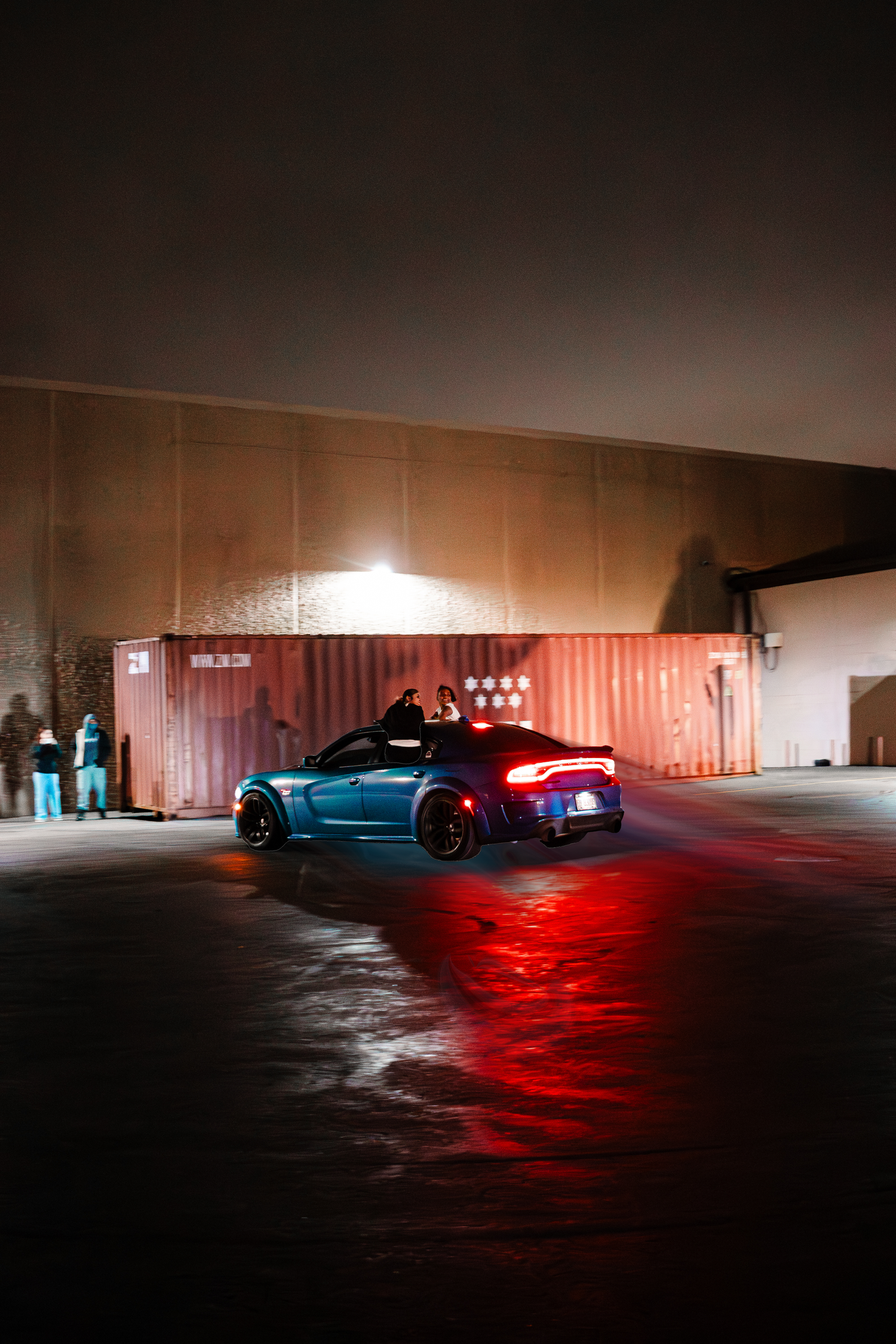 Sports cars parked in dimly lit area with red tail lights reflecting off the ground.